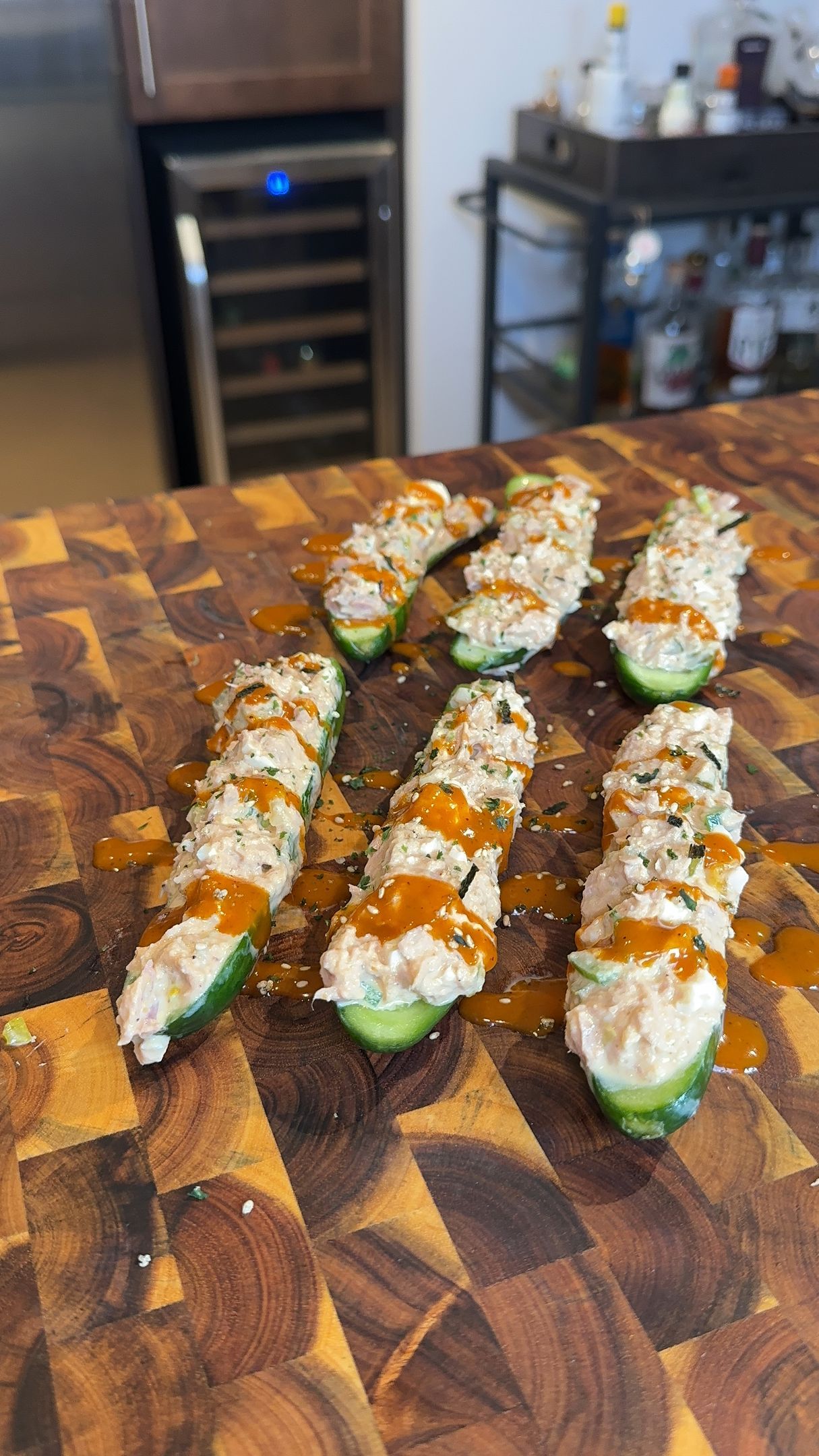 Stuffed cucumber bites with white filling and orange drizzle on a wooden board.