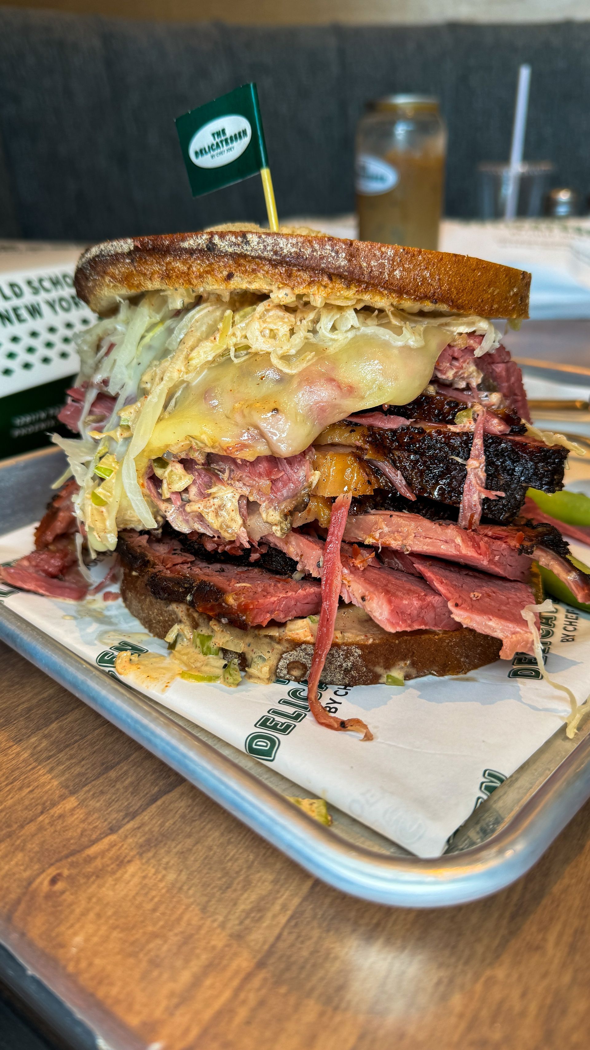 A towering Reuben sandwich on a tray, with corned beef, Swiss cheese, sauerkraut, and rye bread.
