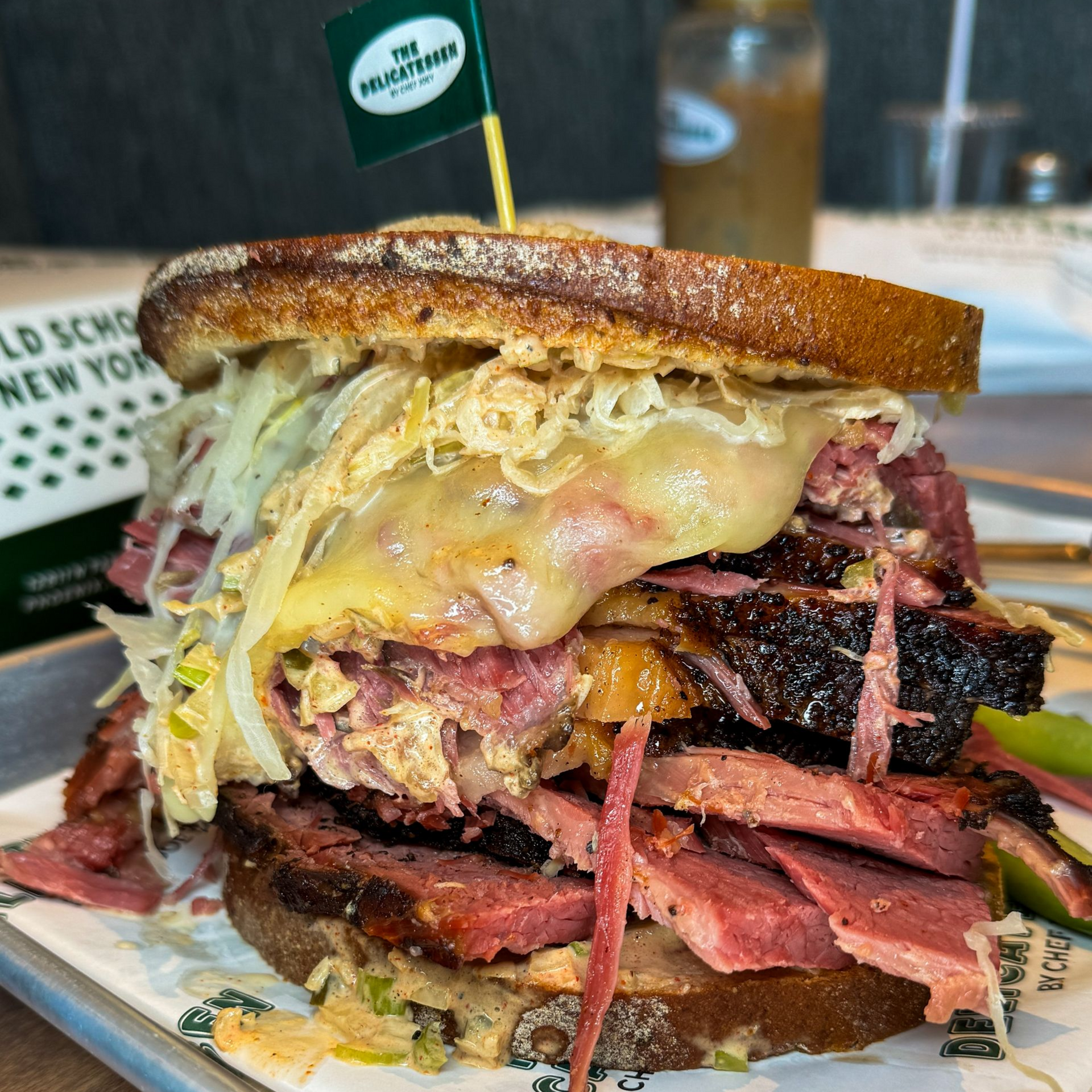 A large, stacked Reuben sandwich on a tray, with sauerkraut, cheese, and pastrami.