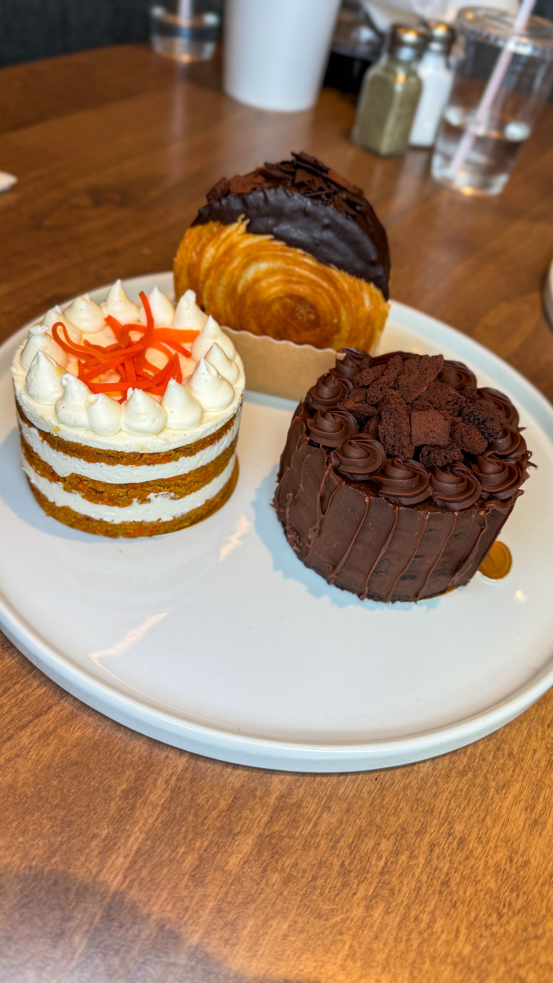 Three desserts on a white plate: carrot cake, chocolate cake, and a pastry.