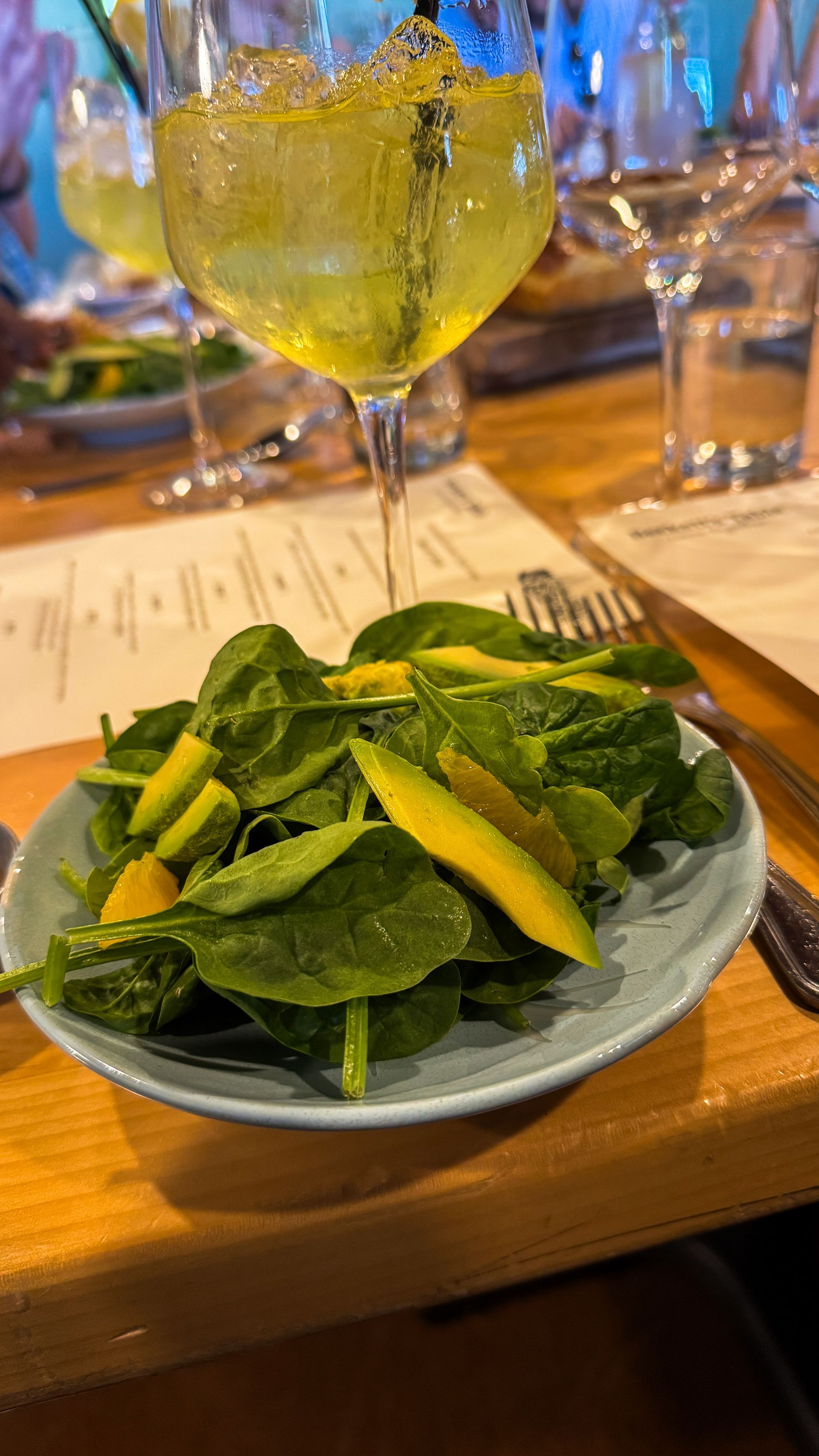 Plate of green salad with lemon wedges on a restaurant table beside a wine glass