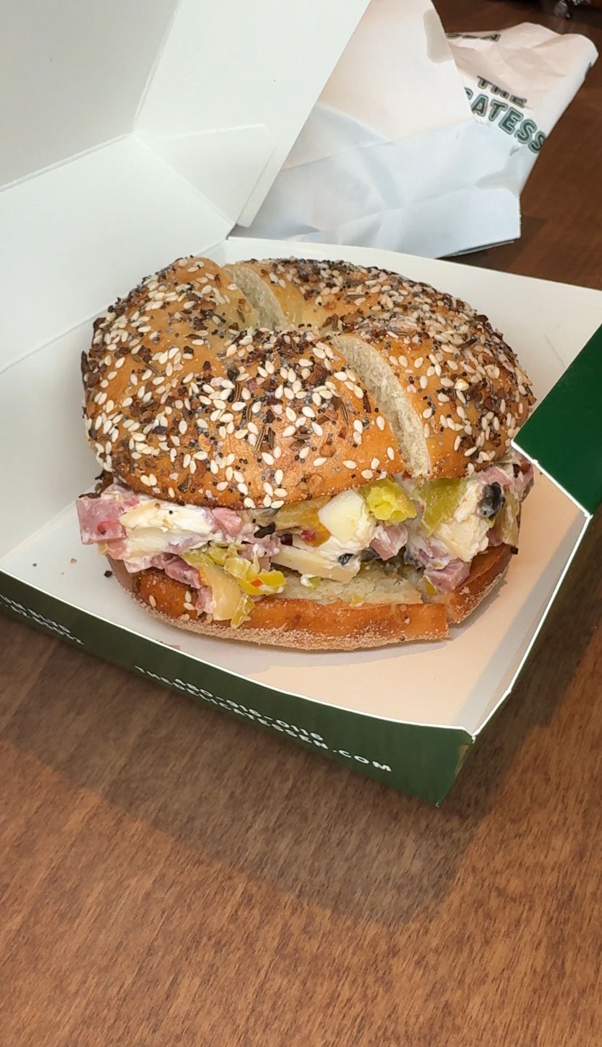 Bagel sandwich in a cardboard box, with seeds on the bagel, and some filling visible.