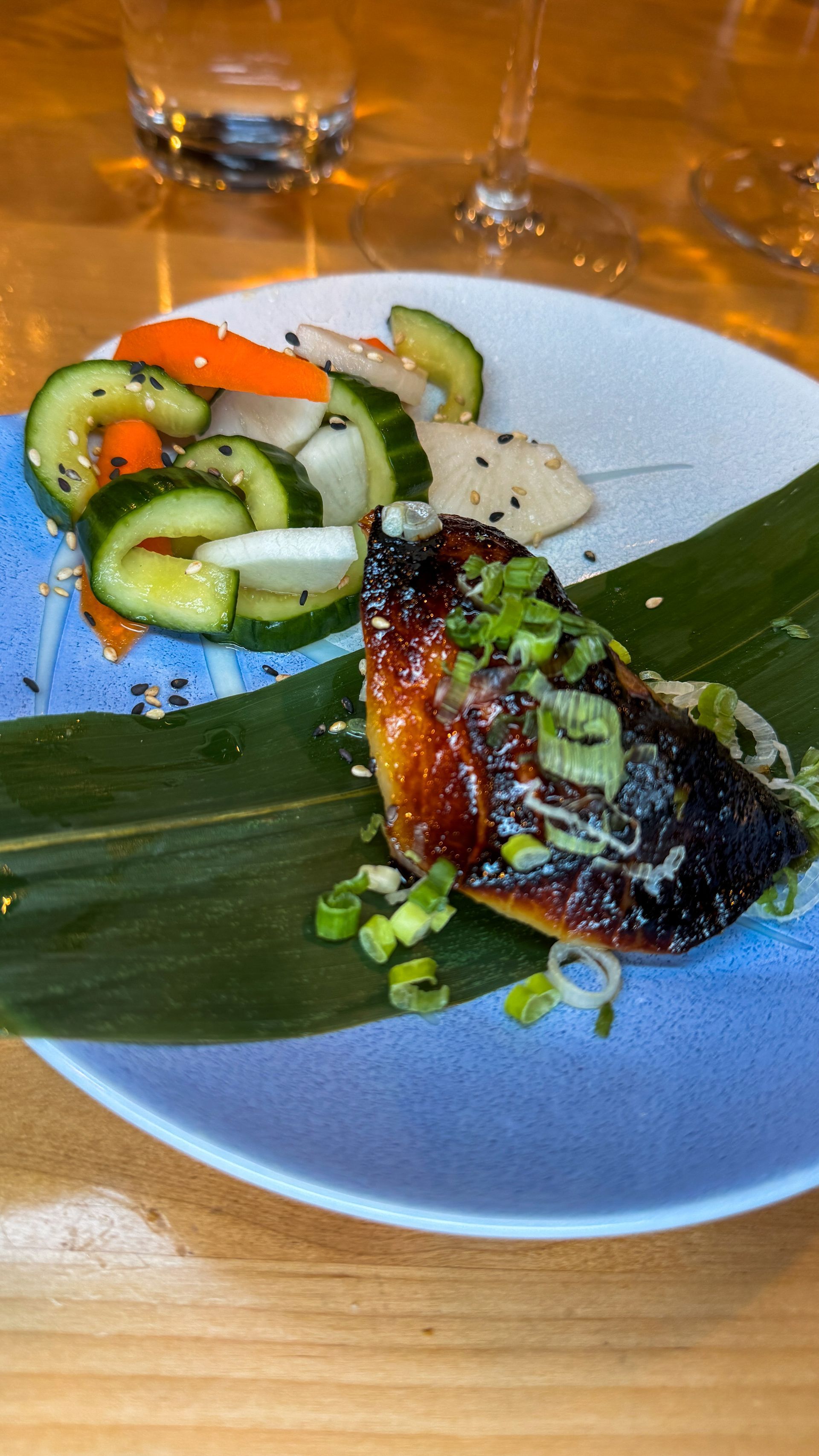 Glazed grilled fish on a banana leaf plate with cucumber salad and a dollop of rice