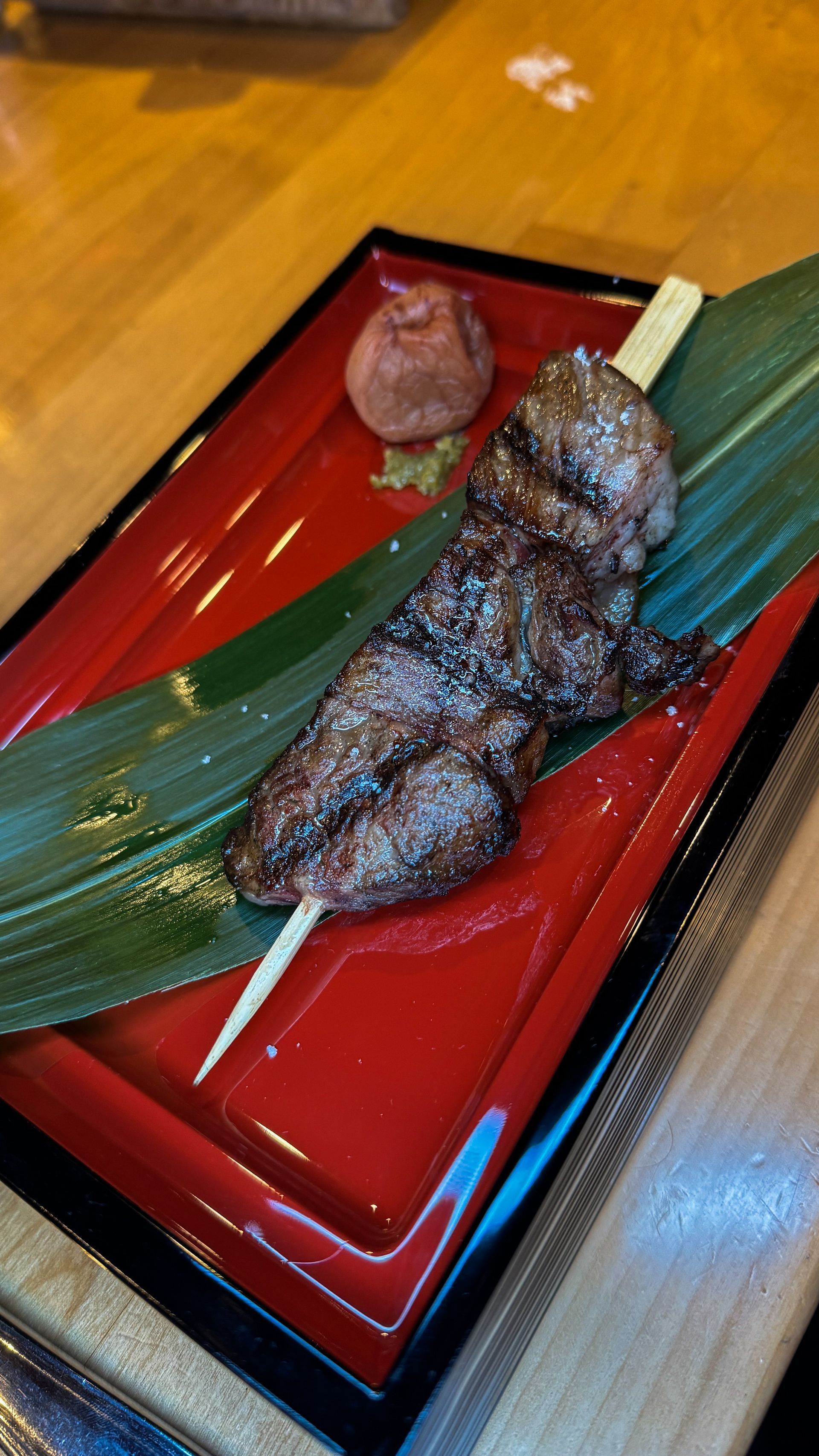 Grilled skewered meat on a red lacquer tray with a small dipping sauce bowl