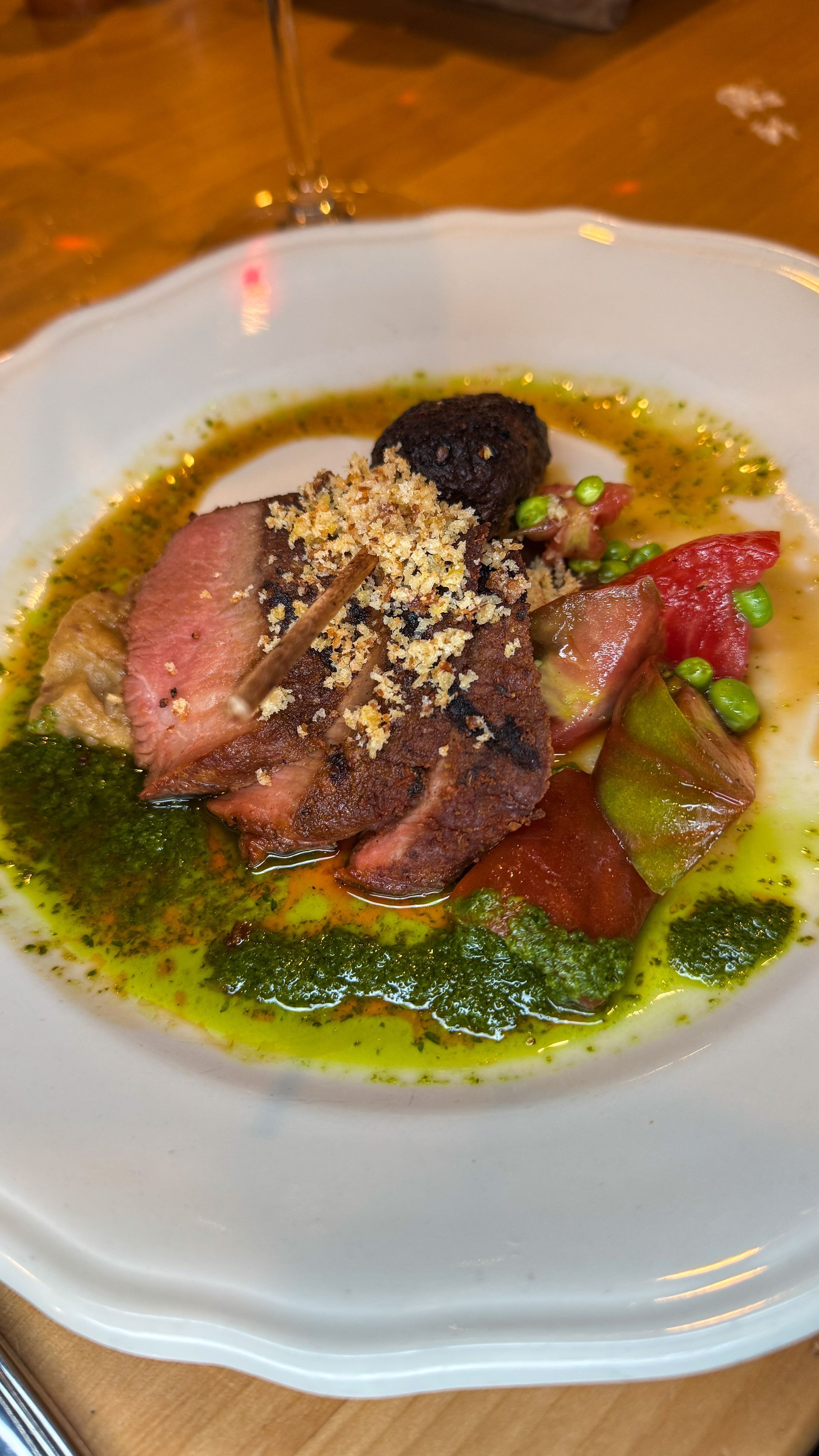 Plated gourmet dish with sliced meat, green sauce, and garnishes on a white plate