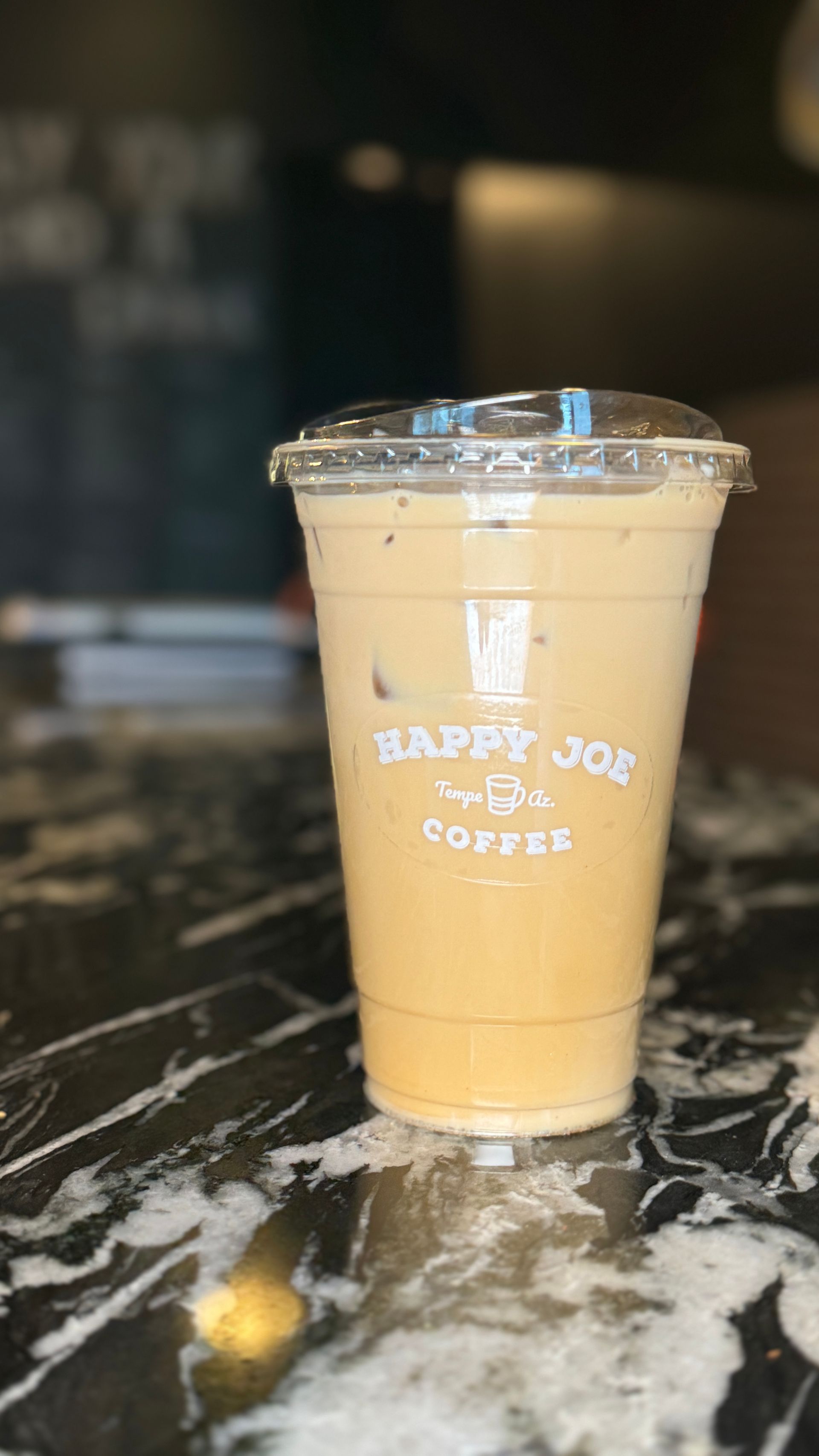 Iced coffee drink in a Happy Joe's Coffee cup on a marble counter.