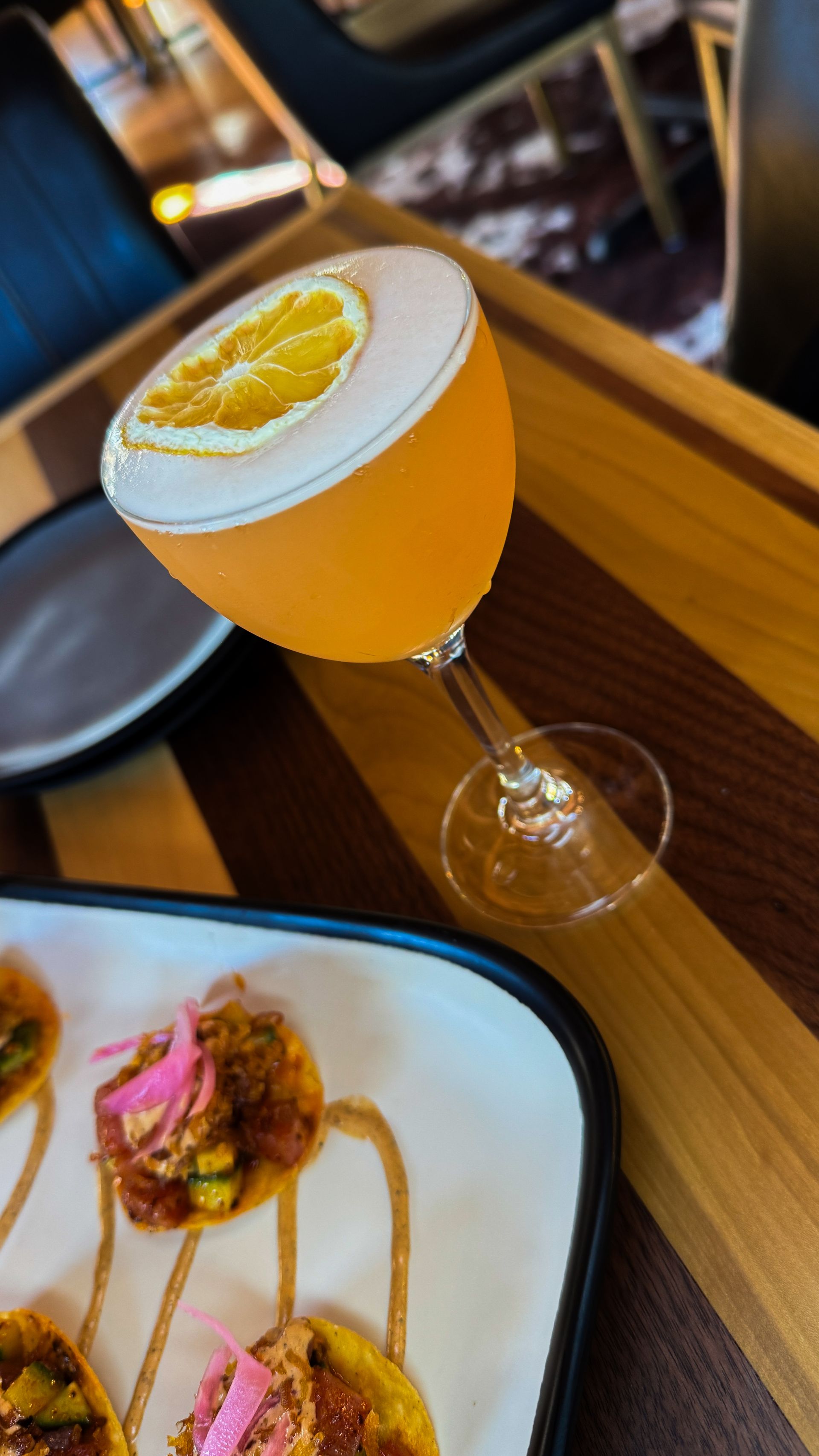 Cocktail with lemon slice in a stemmed glass beside plated food on a restaurant table