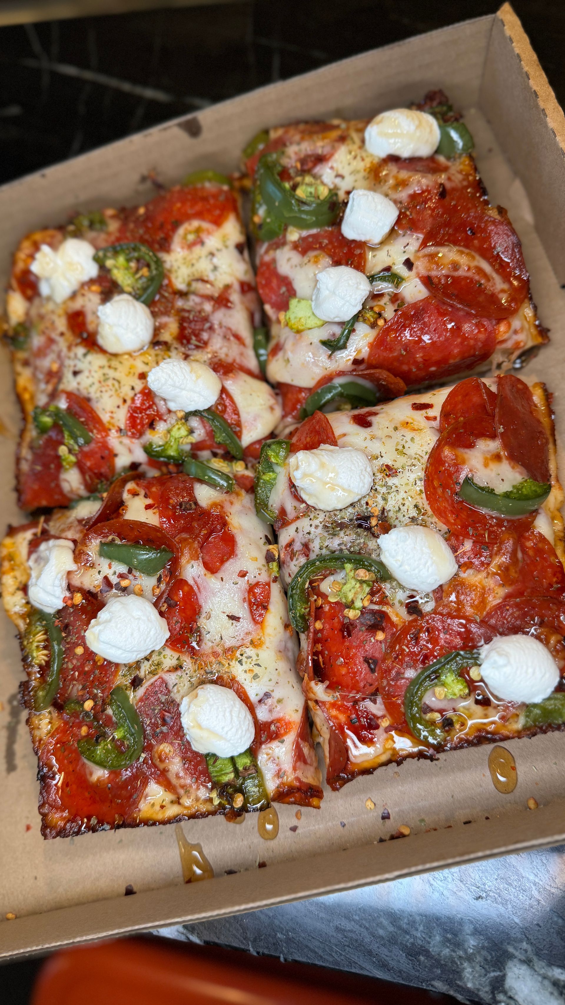 Square pizza slices topped with pepperoni, peppers, and cheese in a cardboard box.