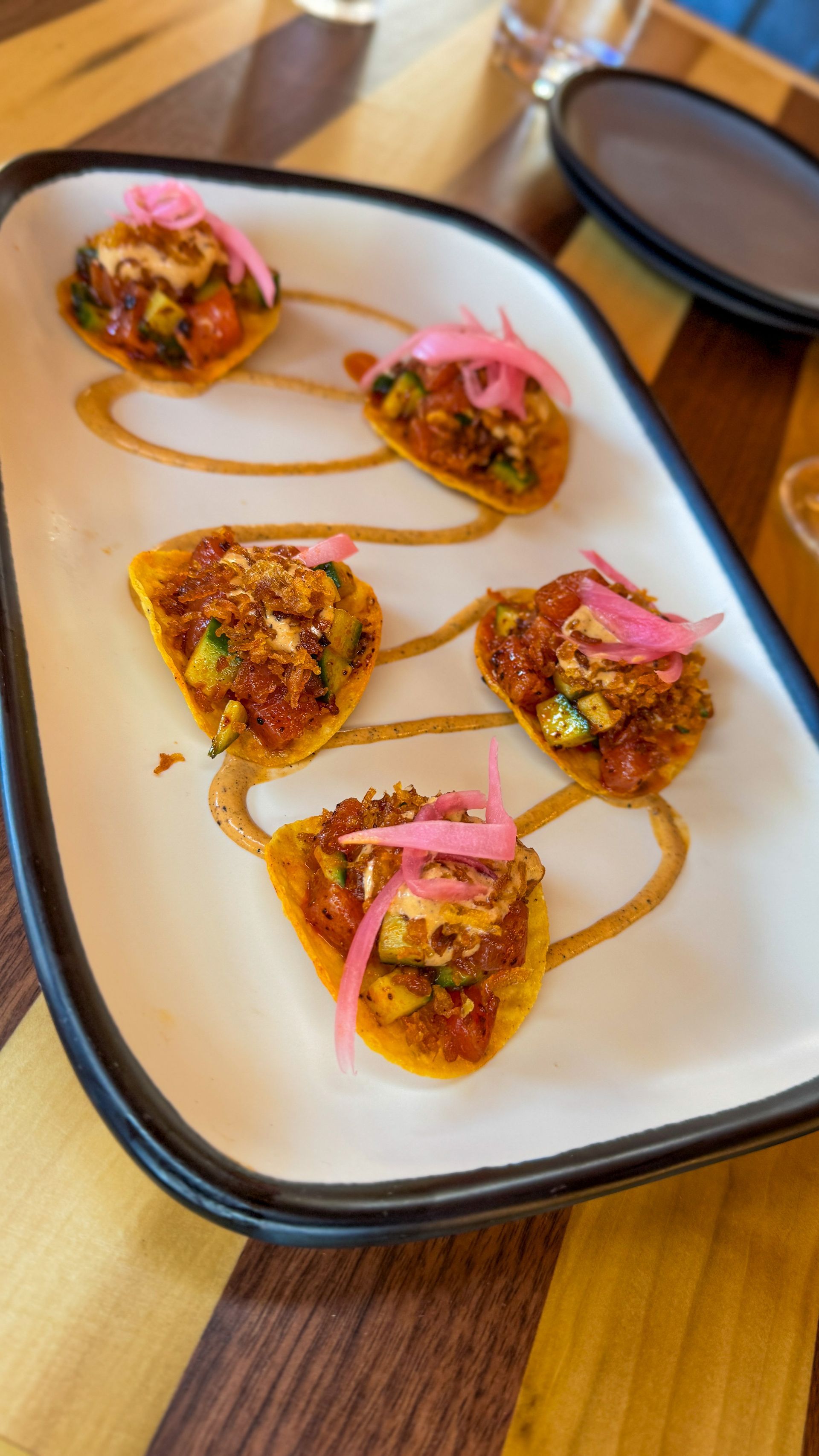 Plated bite-size appetizers topped with pink pickled onions on a white tray on a wooden table