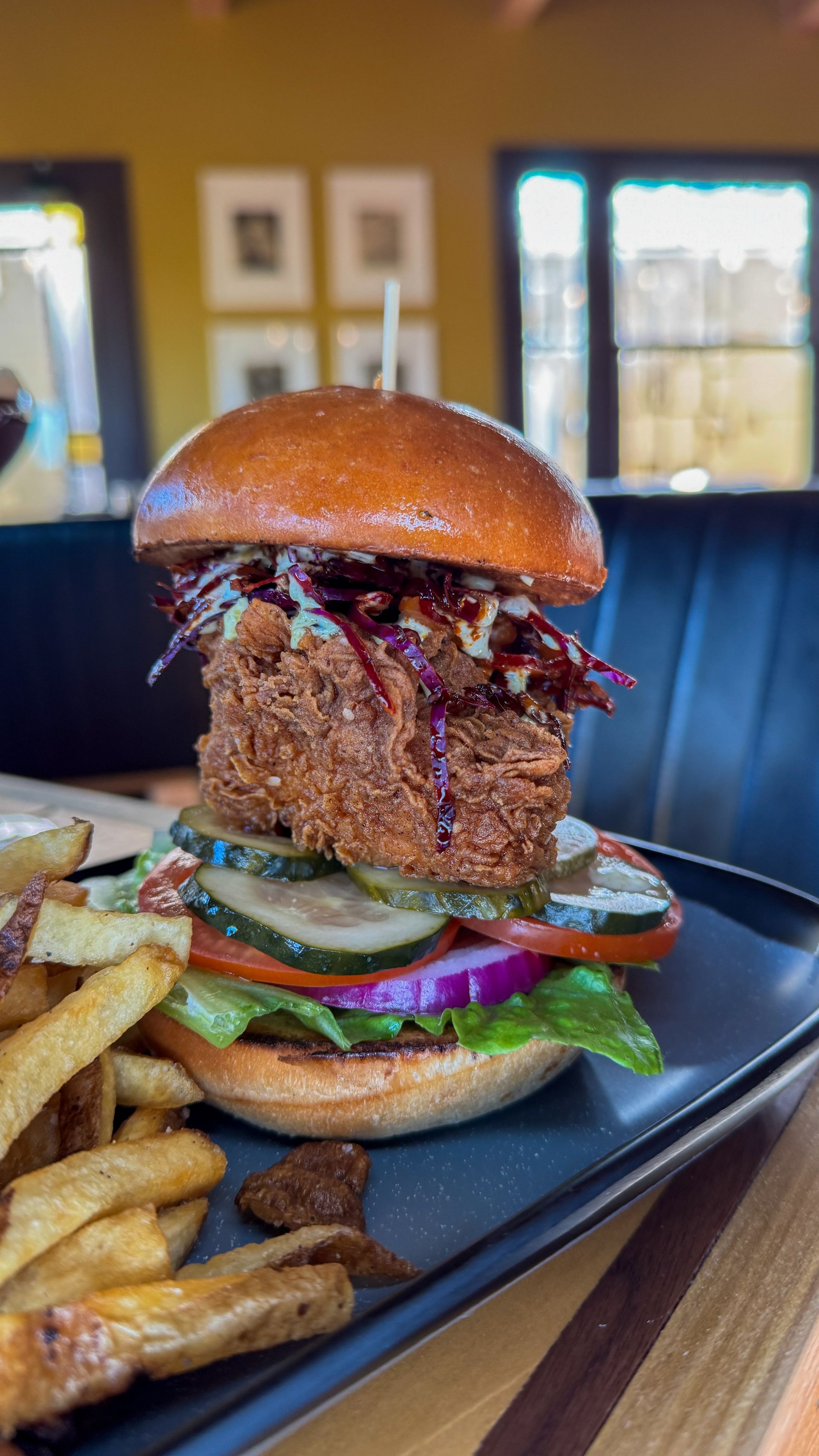 Close-up of a gourmet burger with fries on a black plate in a restaurant.