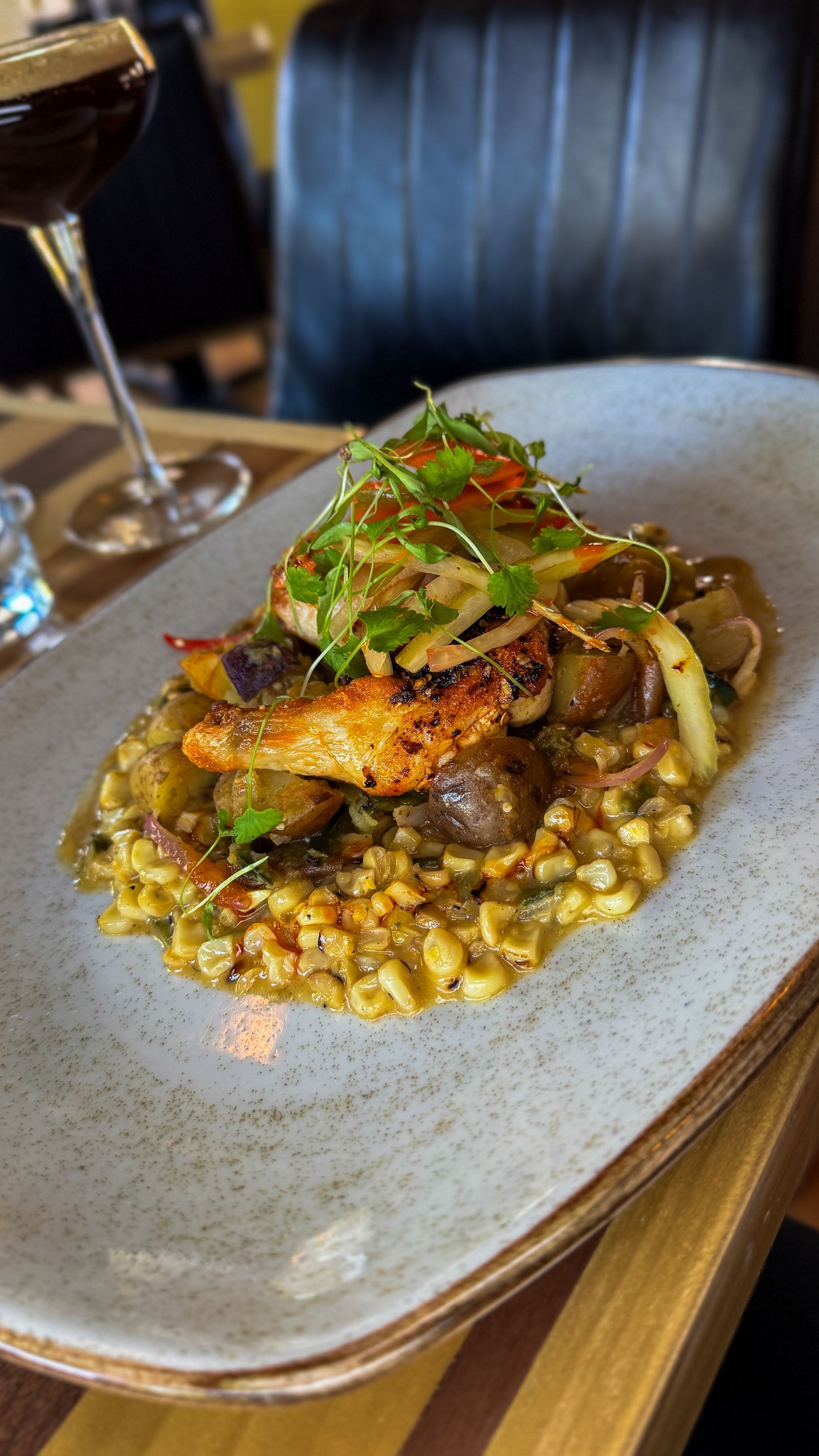 Gourmet plated dish with corn, mushrooms, and herbs on a gray plate in a dim restaurant setting