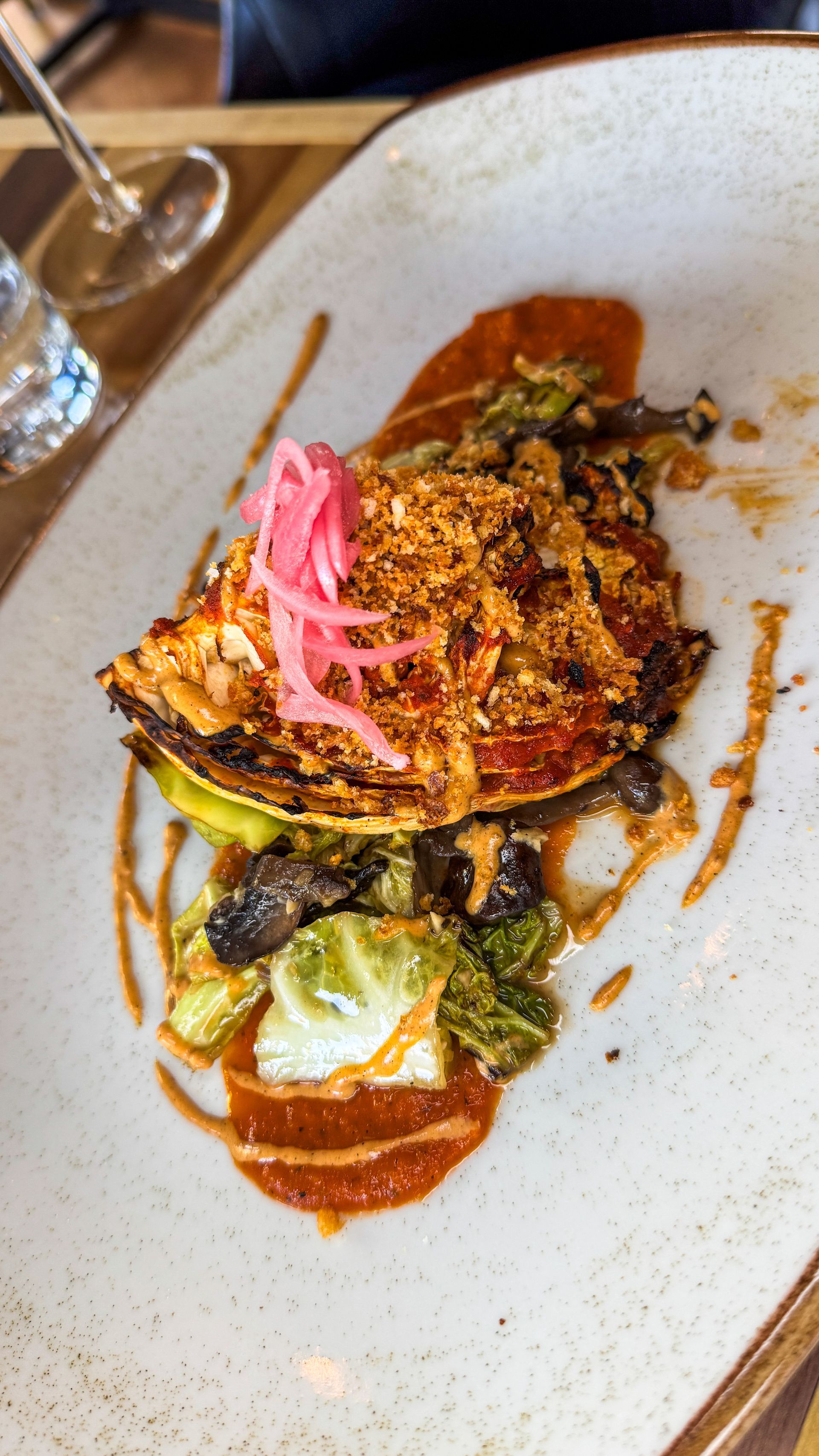 Plated gourmet dish with sauce and pickled pink garnish on a white plate at a table