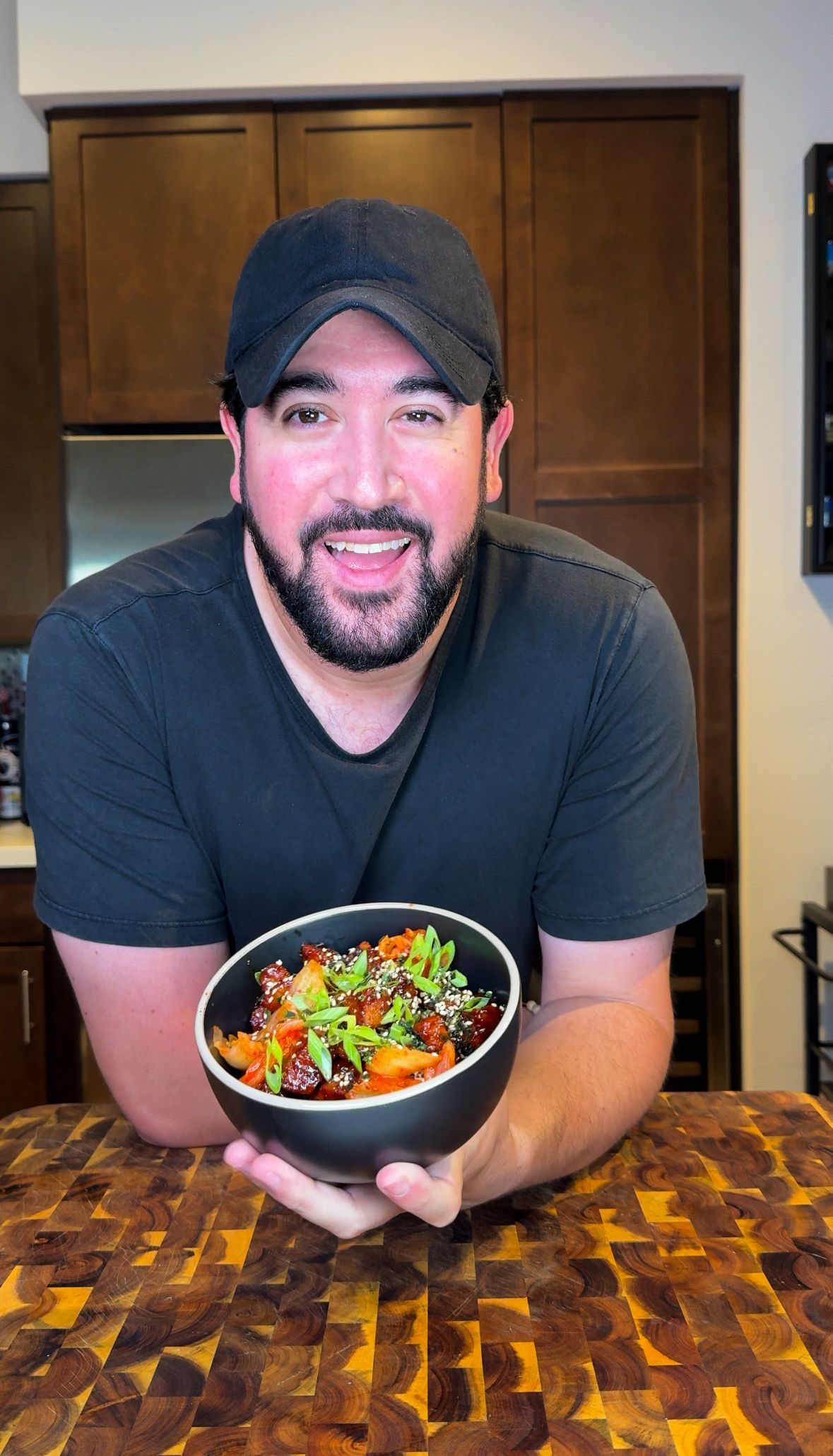 Man holding a tray of loaded nachos, brown cabinets in background, excited expression.