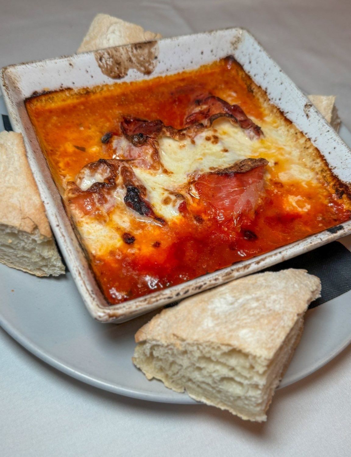 A white plate topped with a casserole and bread on a table.