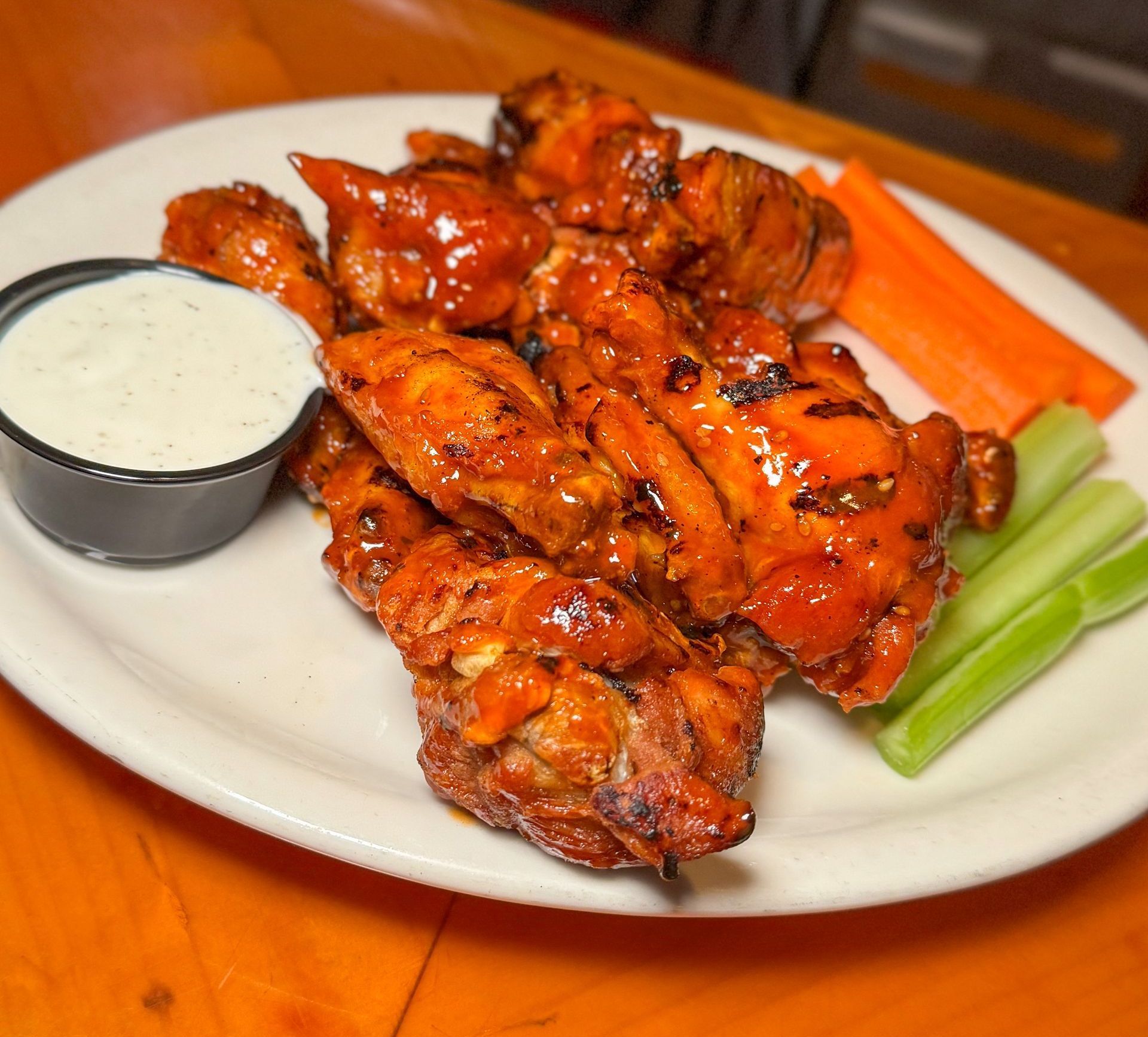 A white plate topped with chicken wings , carrots , celery and ranch dressing.
