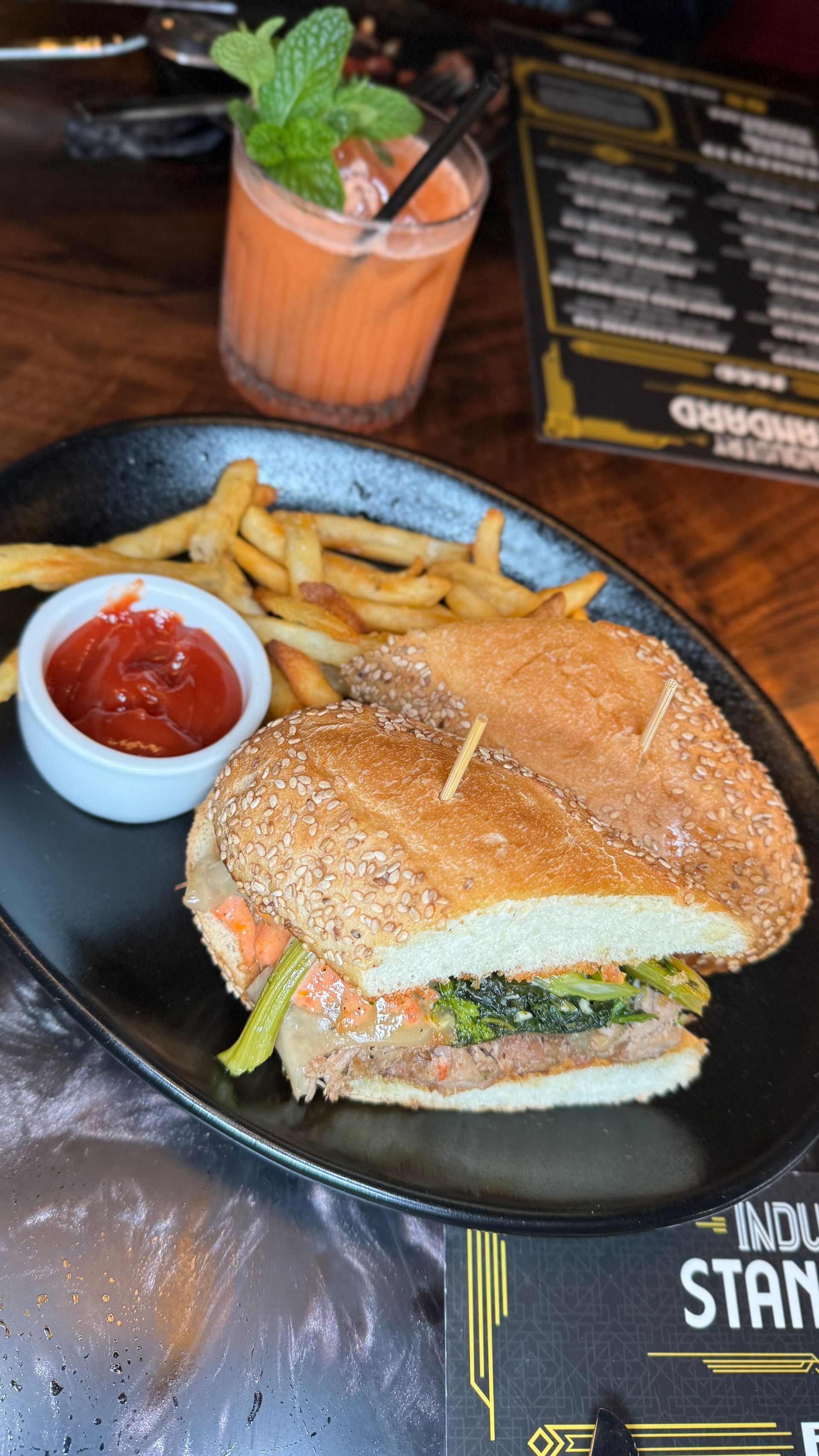 A sandwich and french fries on a black plate on a table.