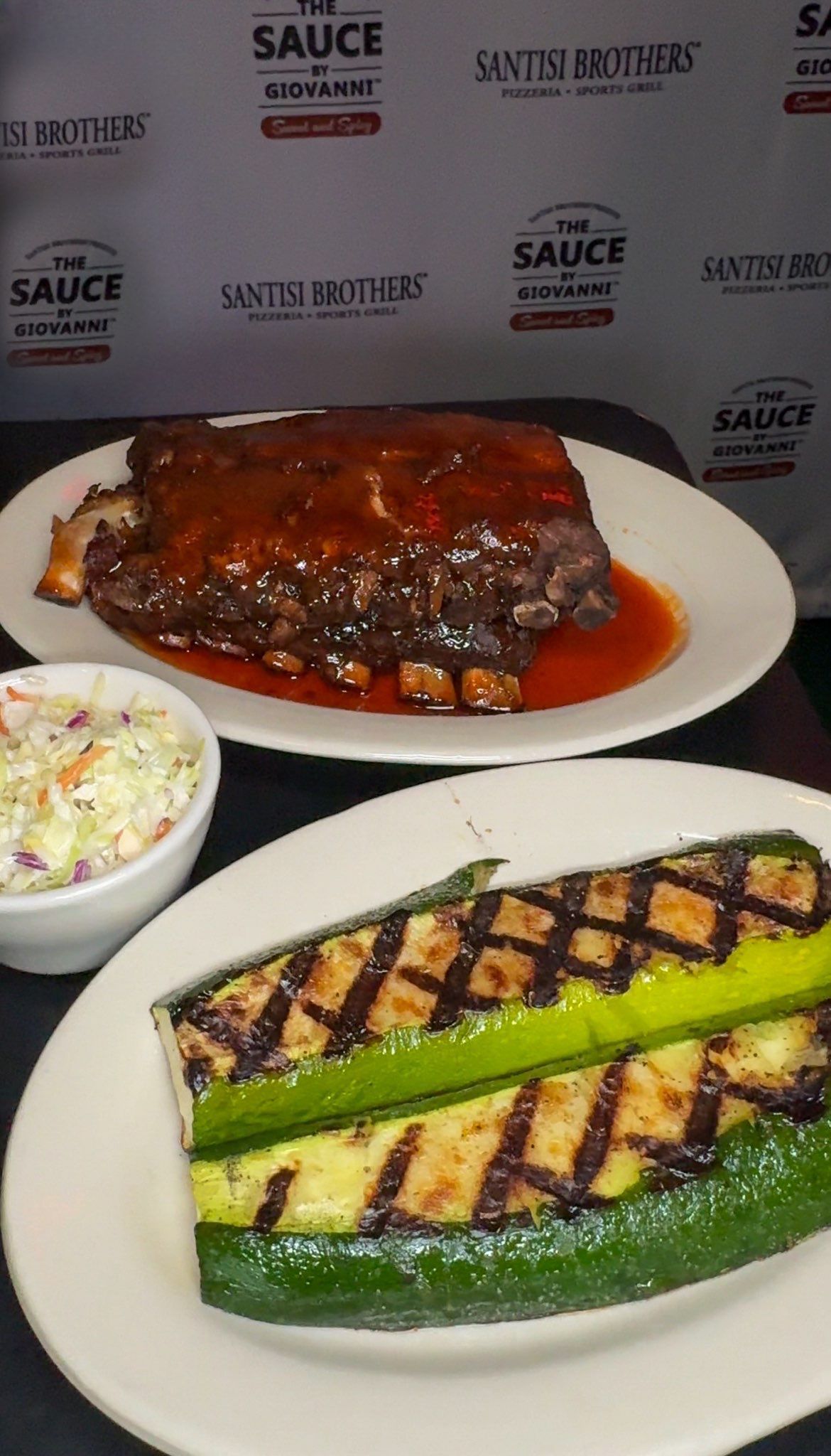 A plate of ribs and a plate of grilled zucchini are on a table.