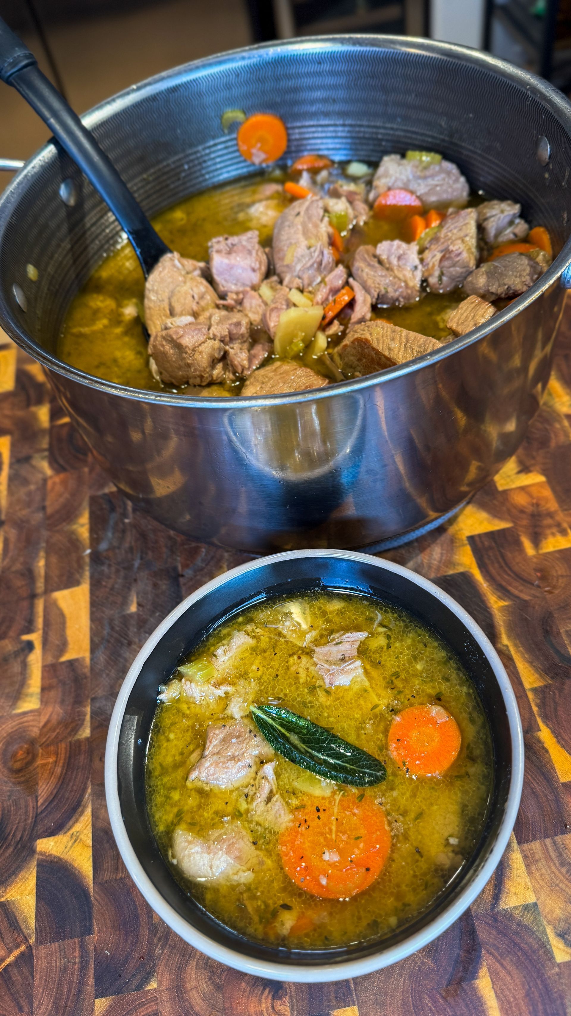 Pot of stew with carrots and meat, served in a black bowl.