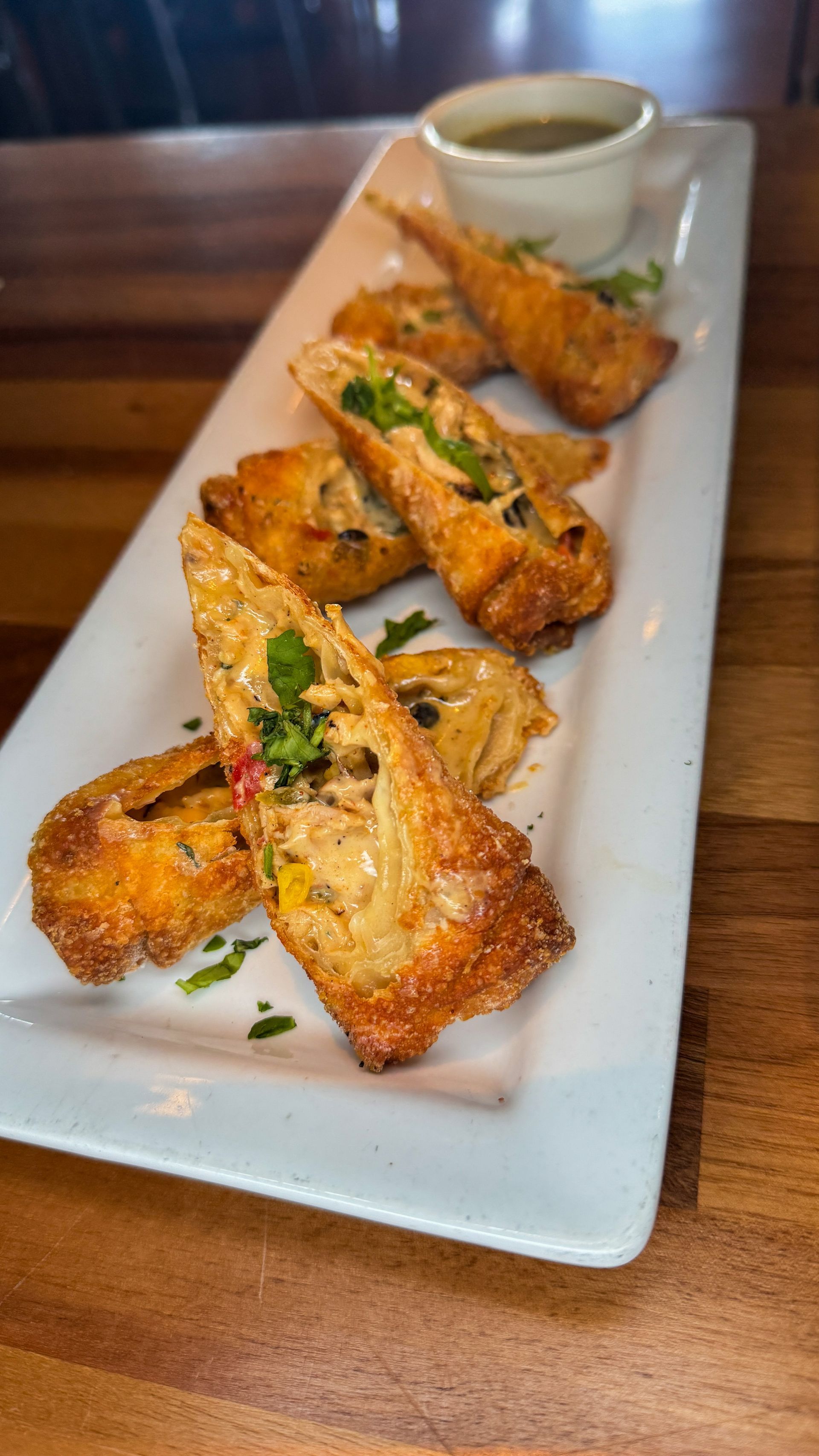 Fried, golden-brown egg rolls on a white rectangular plate, with a small bowl of dipping sauce.
