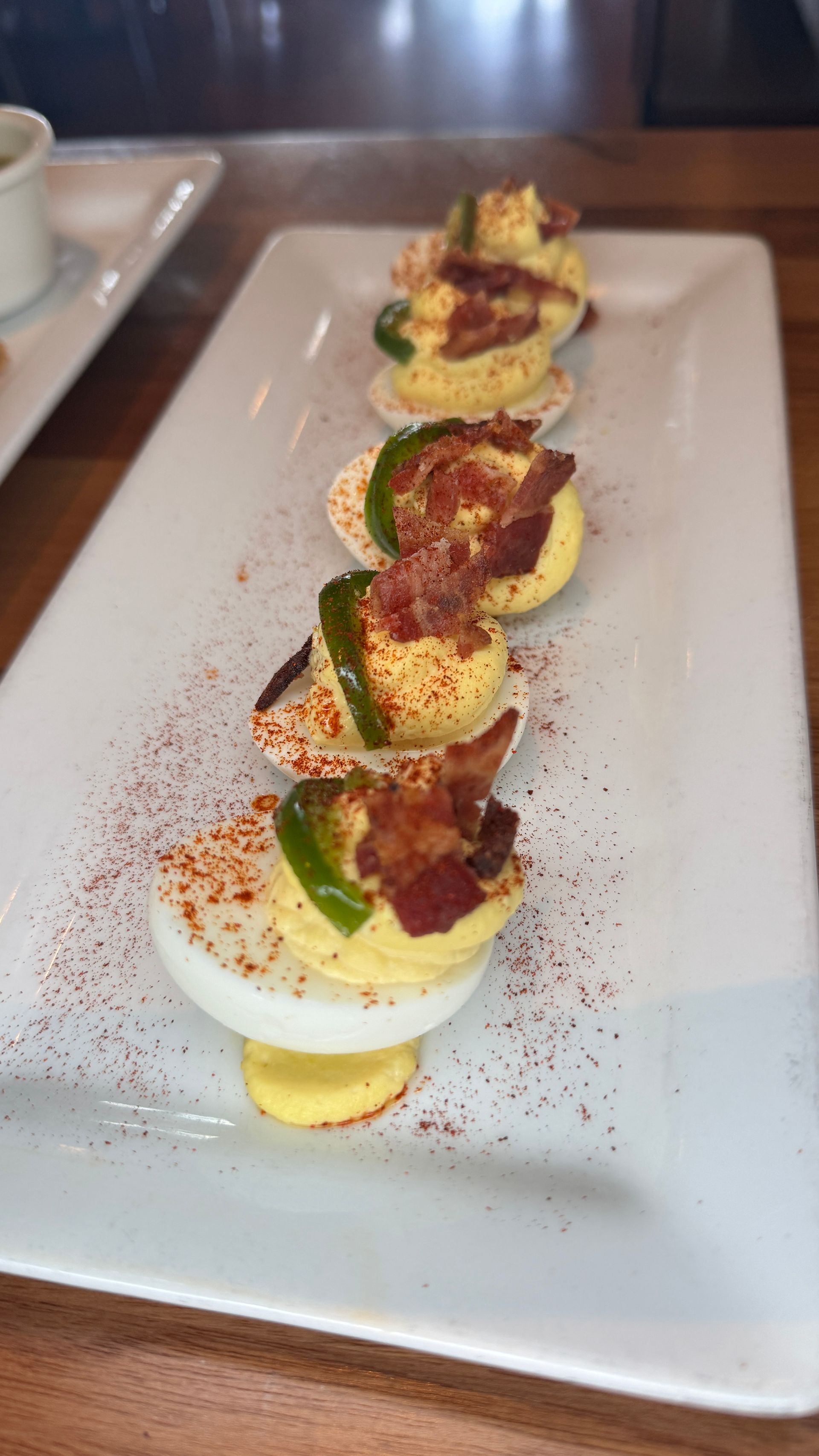 Deviled eggs on a white rectangular plate; topped with bacon, jalapeño, and paprika.