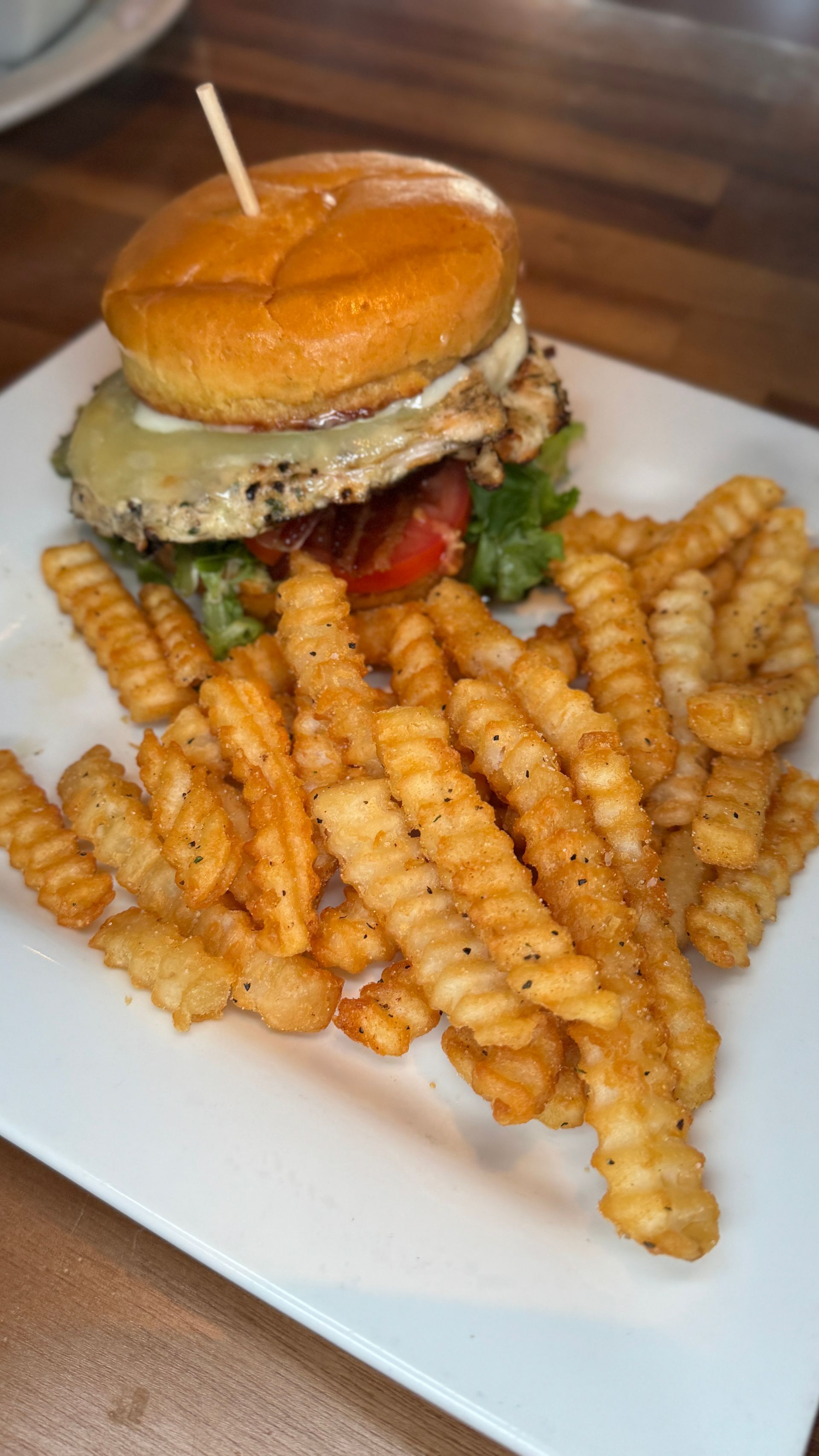 Burger on a bun with lettuce, tomato, and fries on a white plate.