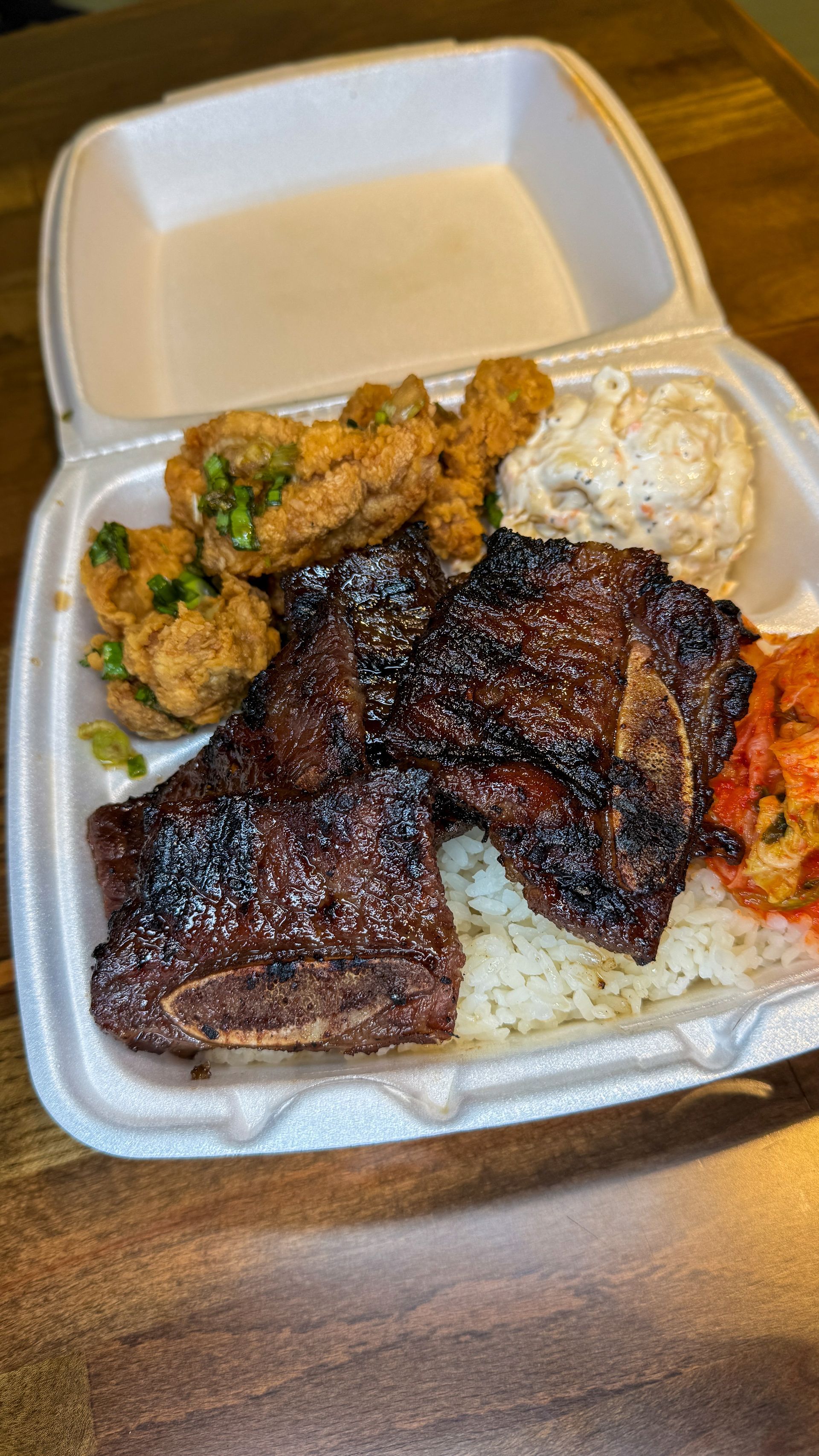 Grilled meat and side dishes in a takeout container.