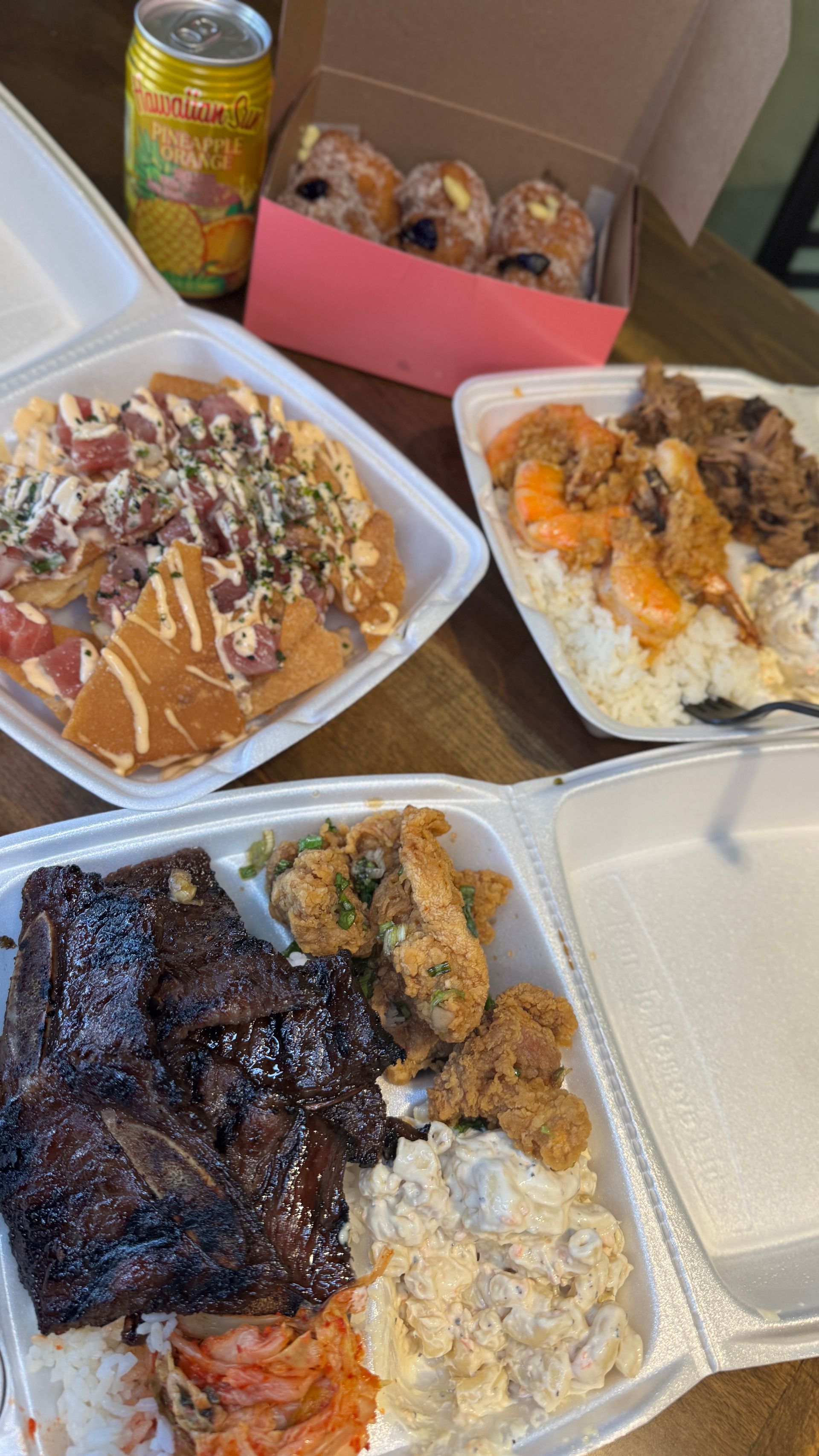 Food containers with various dishes: ribs, shrimp, nachos, and muffins. A can of juice.