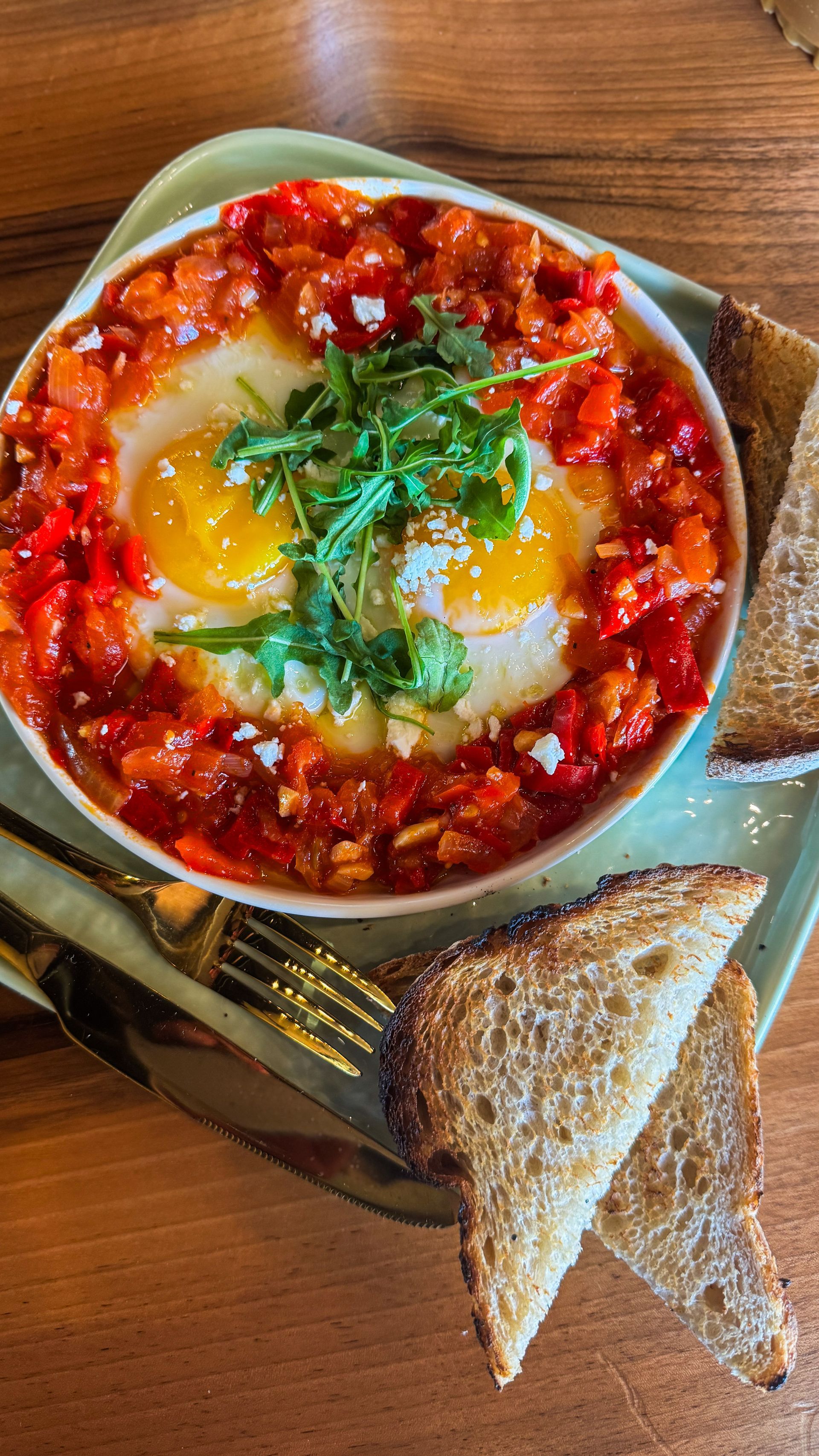 Shakshuka with two sunny-side-up eggs, red sauce, herbs, and toasted bread on a plate.