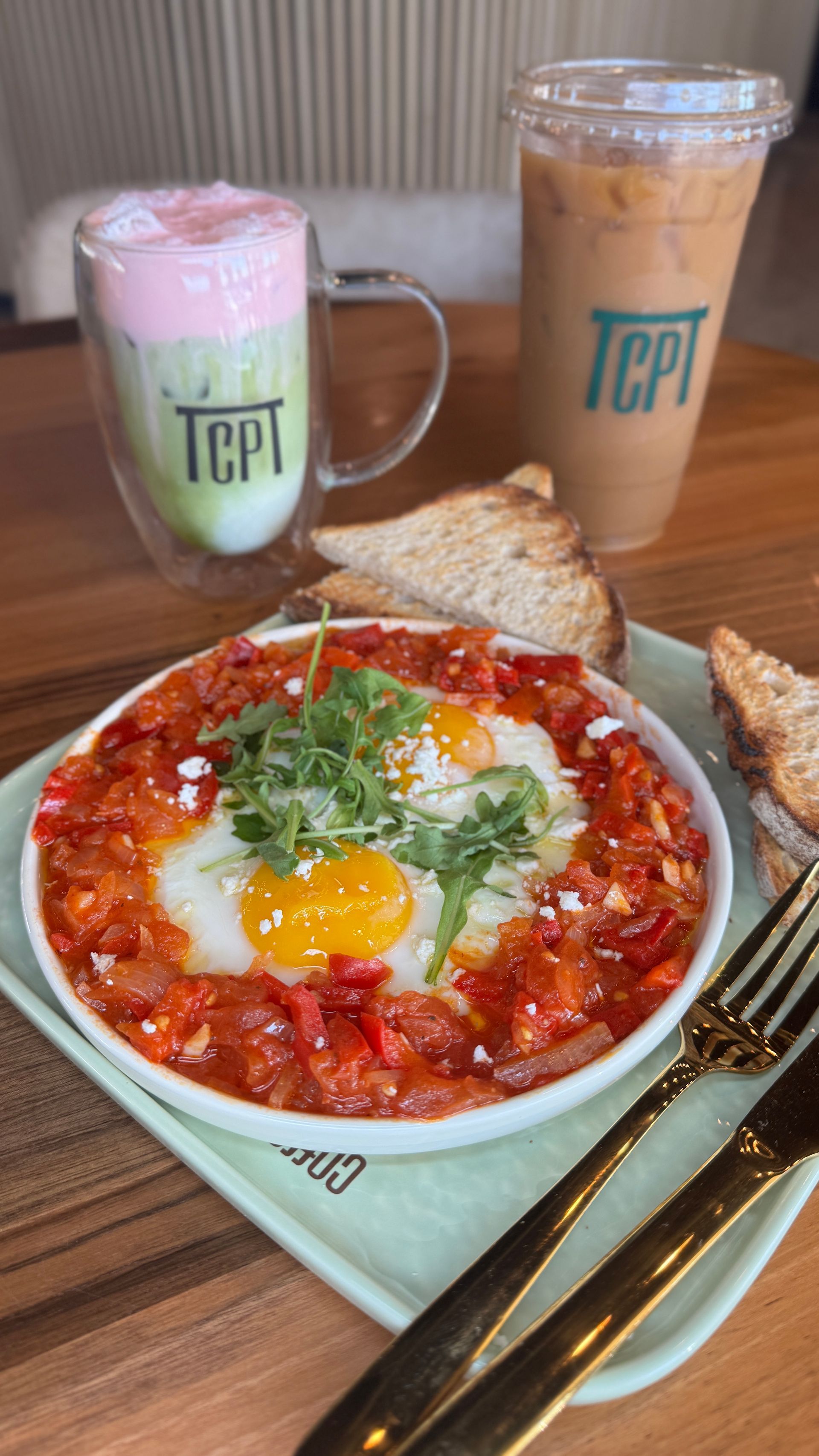 Breakfast plate with eggs in tomato sauce, toast, and two drinks.