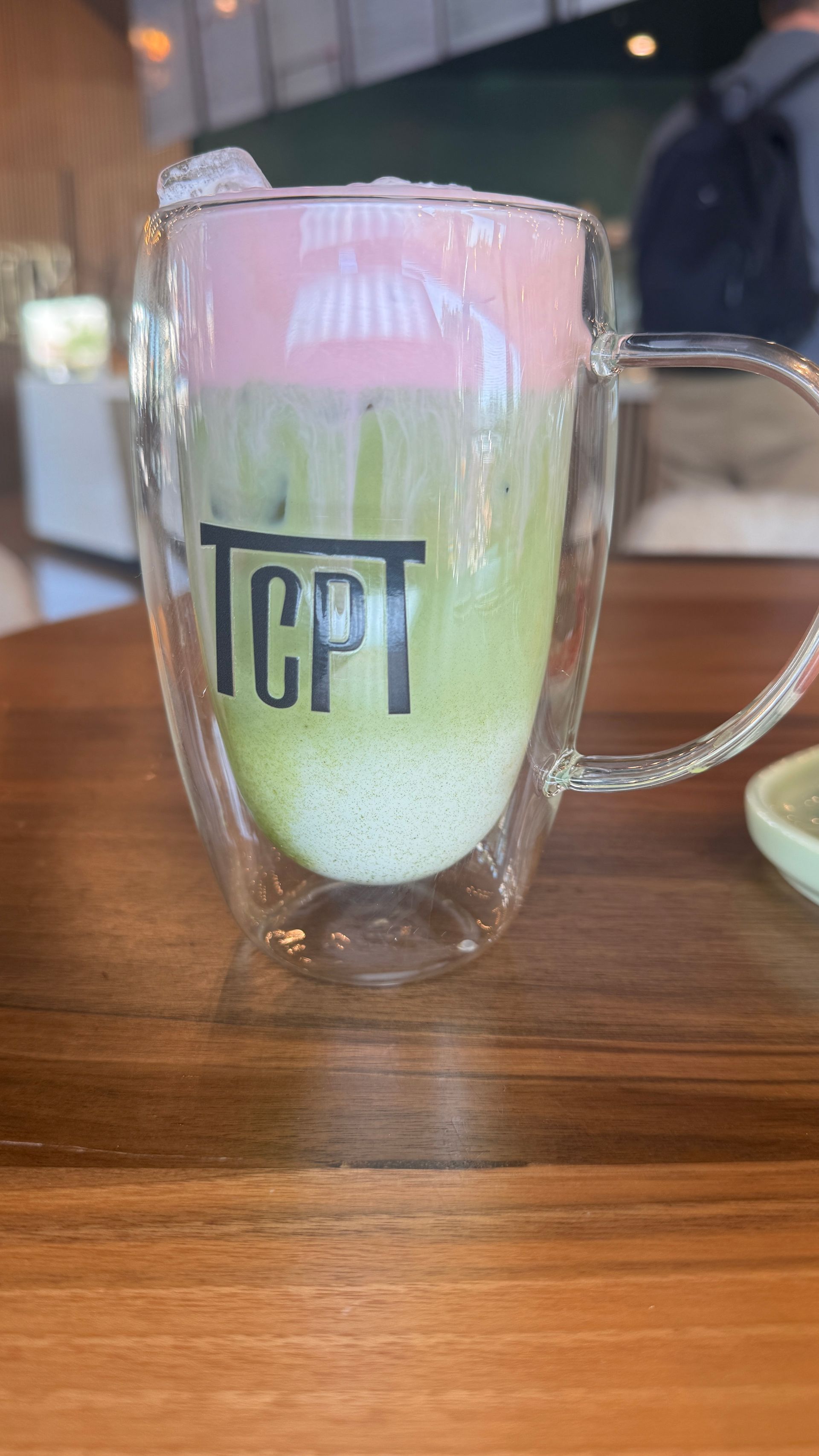 Layered matcha latte with pink foam in a glass mug on a wooden table.