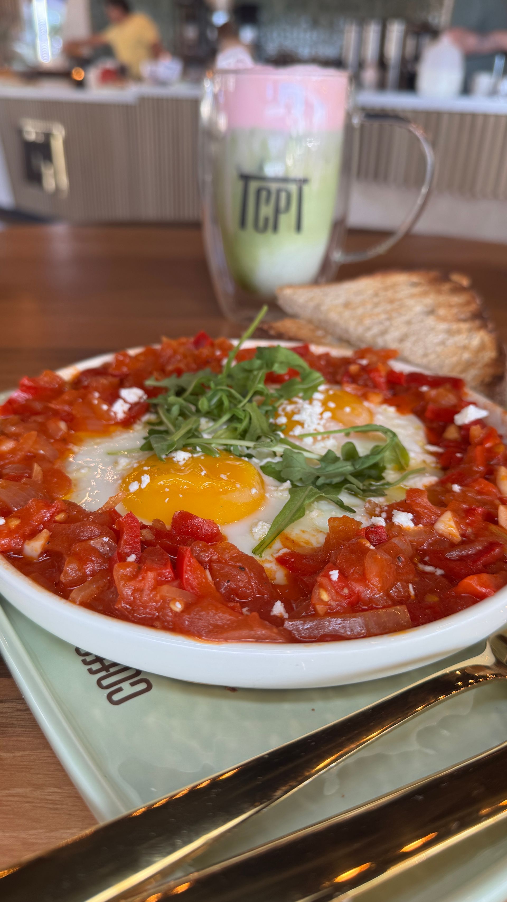 Eggs in tomato sauce with arugula, feta, toast, and a green latte.