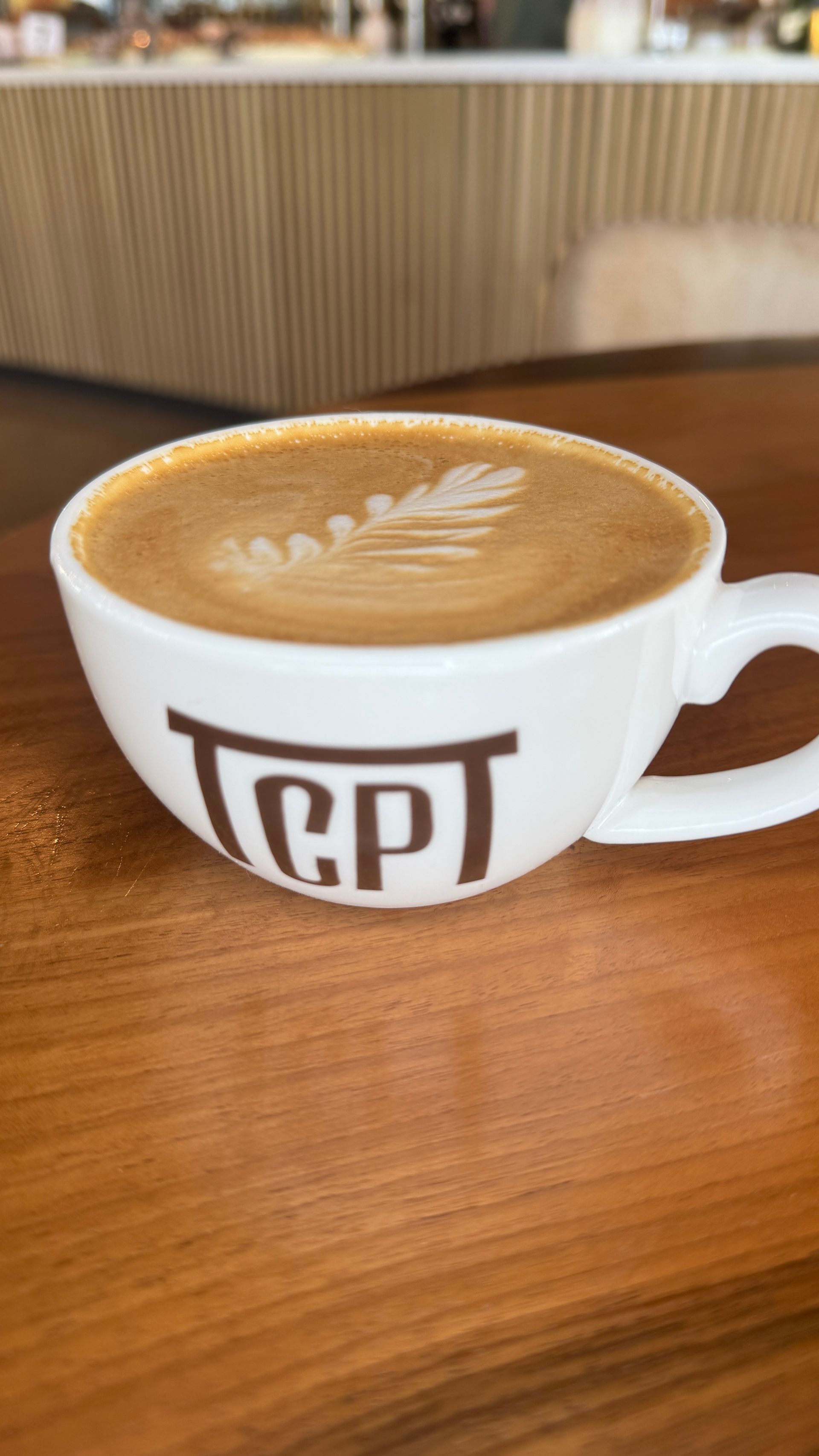Latte in a white mug on a wooden table, featuring leaf art, with