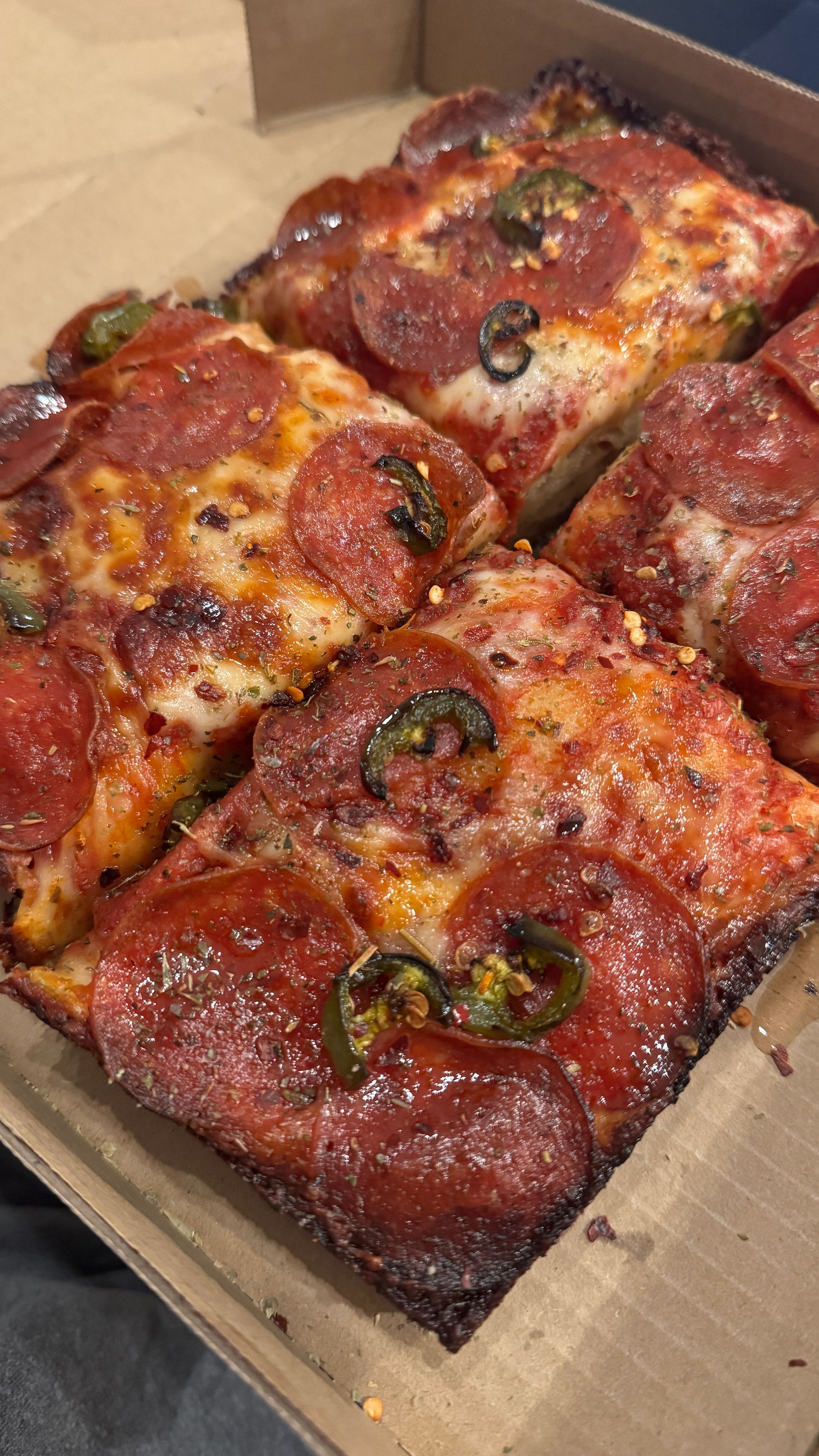 Square pepperoni pizza with jalapeños in a cardboard box, close-up.