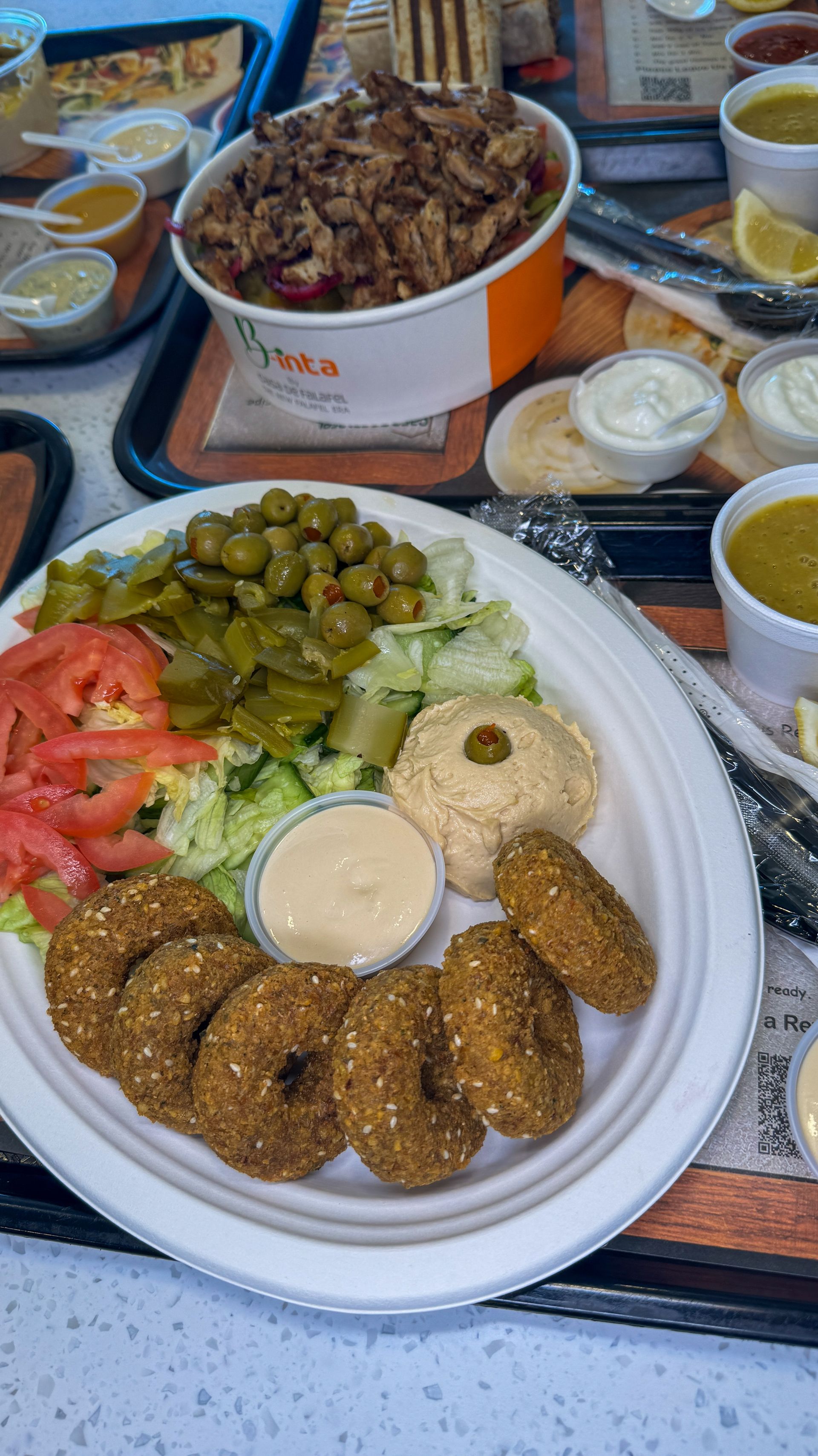 Falafel platter with hummus, olives, tomatoes, and tahini, alongside a container of shawarma.