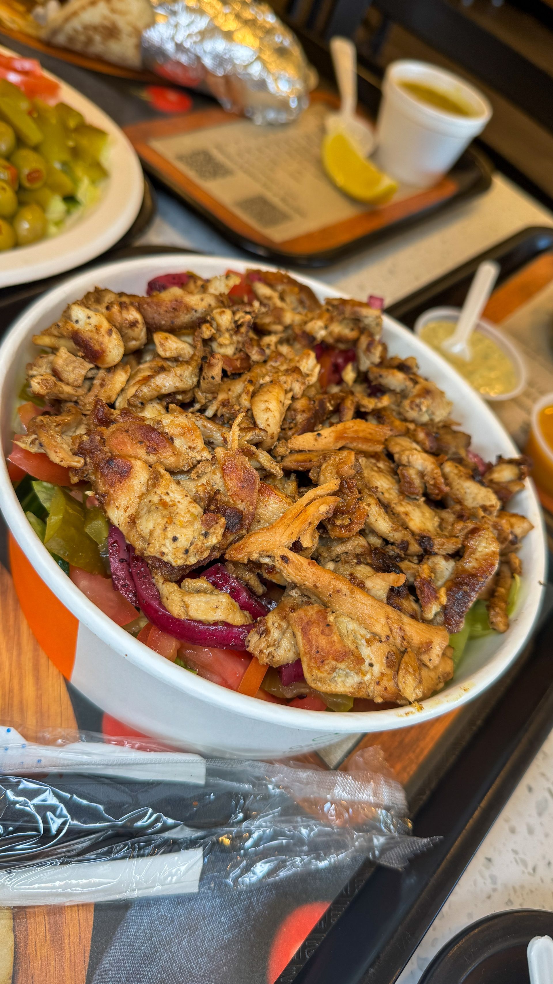 Bowl of seasoned chicken over salad, other food items visible in background.