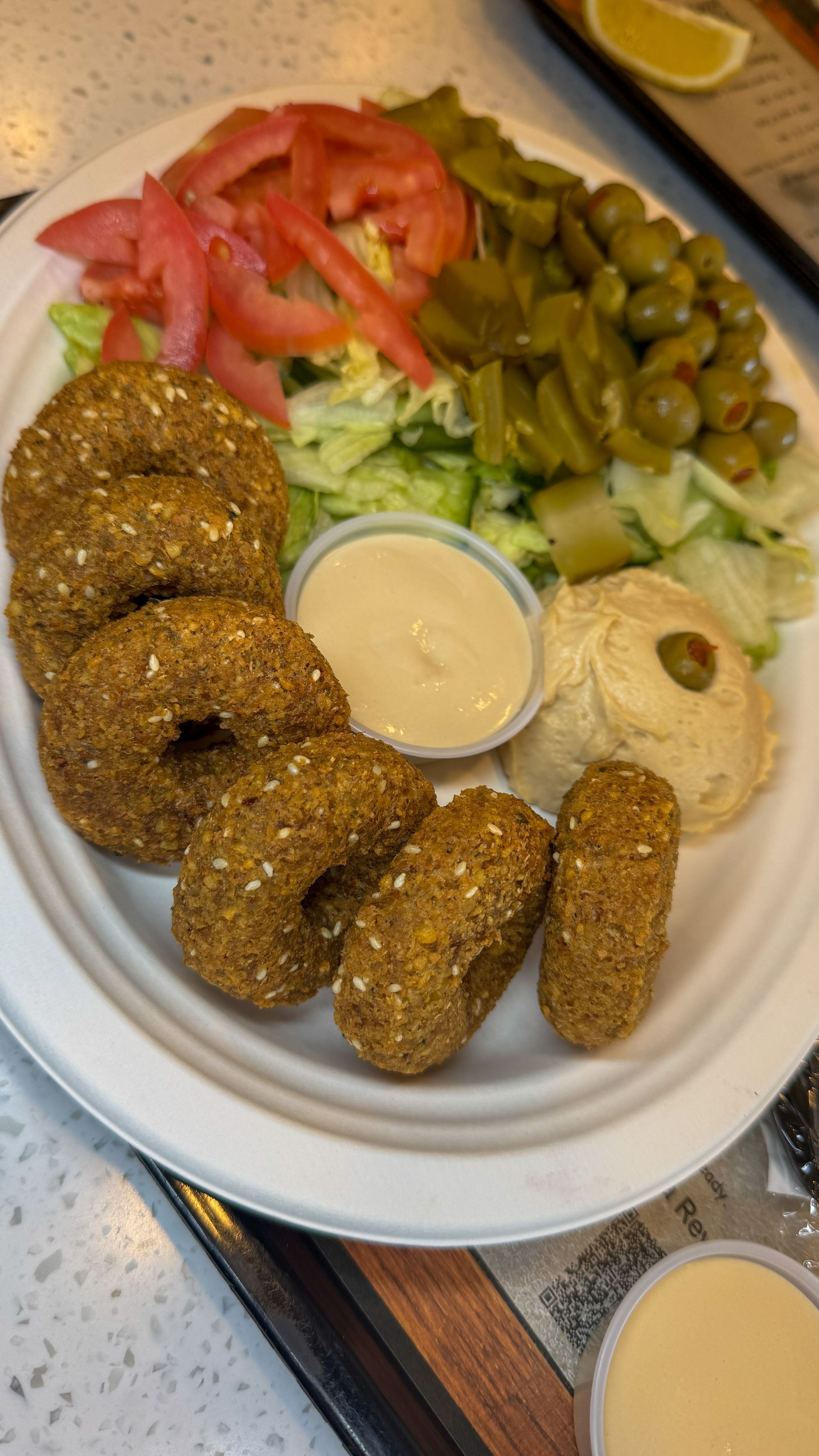Plate of falafel, hummus, salad, olives, pickled vegetables, and tahini sauce.