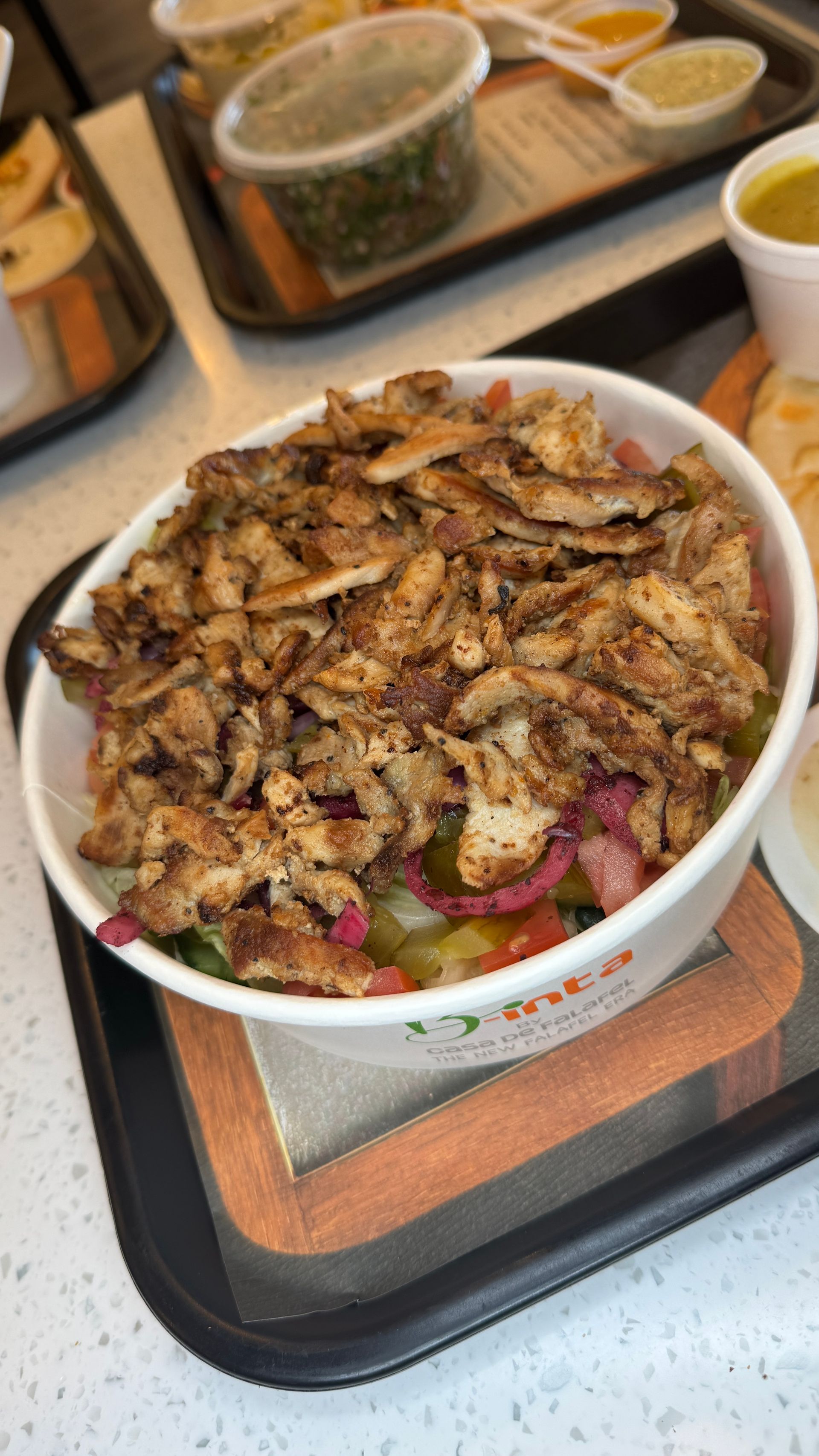 Bowl of food with shredded meat, vegetables, and other sides on a tray.
