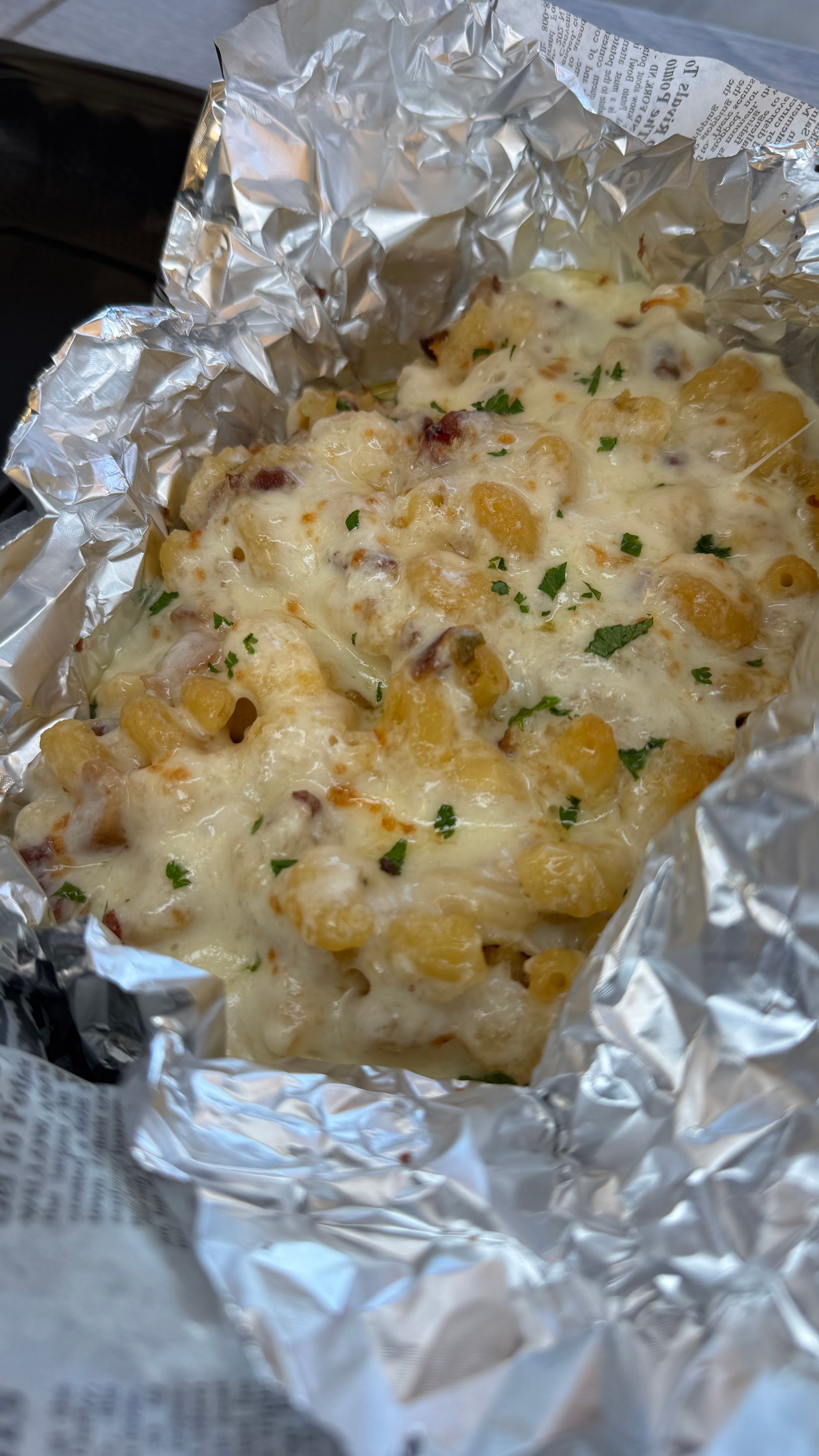Foil-wrapped cheesy baked potato topped with herbs and bits of bacon