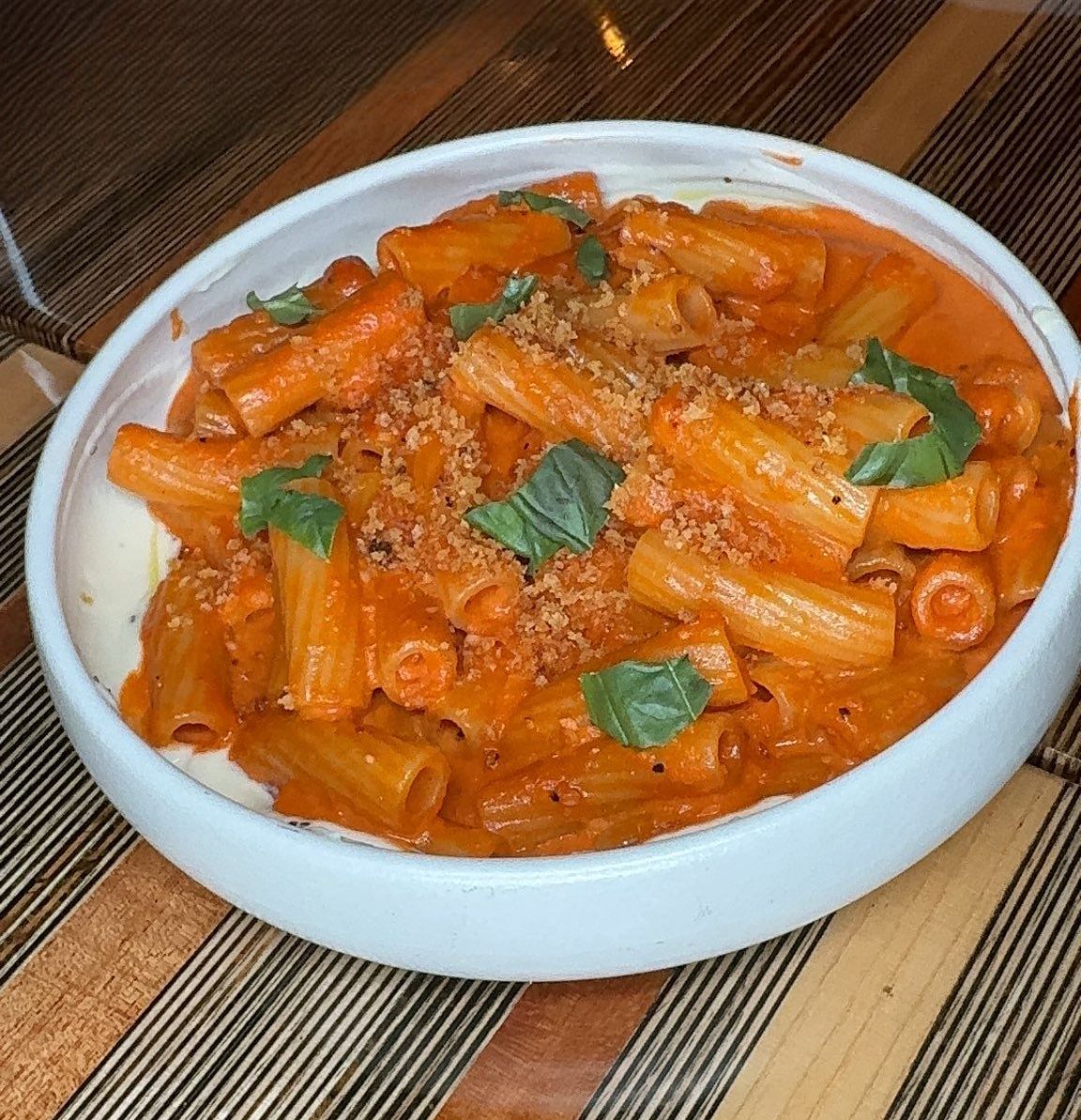 A white bowl filled with pasta and sauce on a table