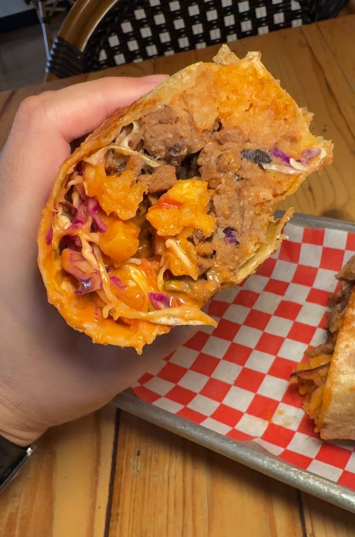A person is holding a burrito with meat and coleslaw in their hand.