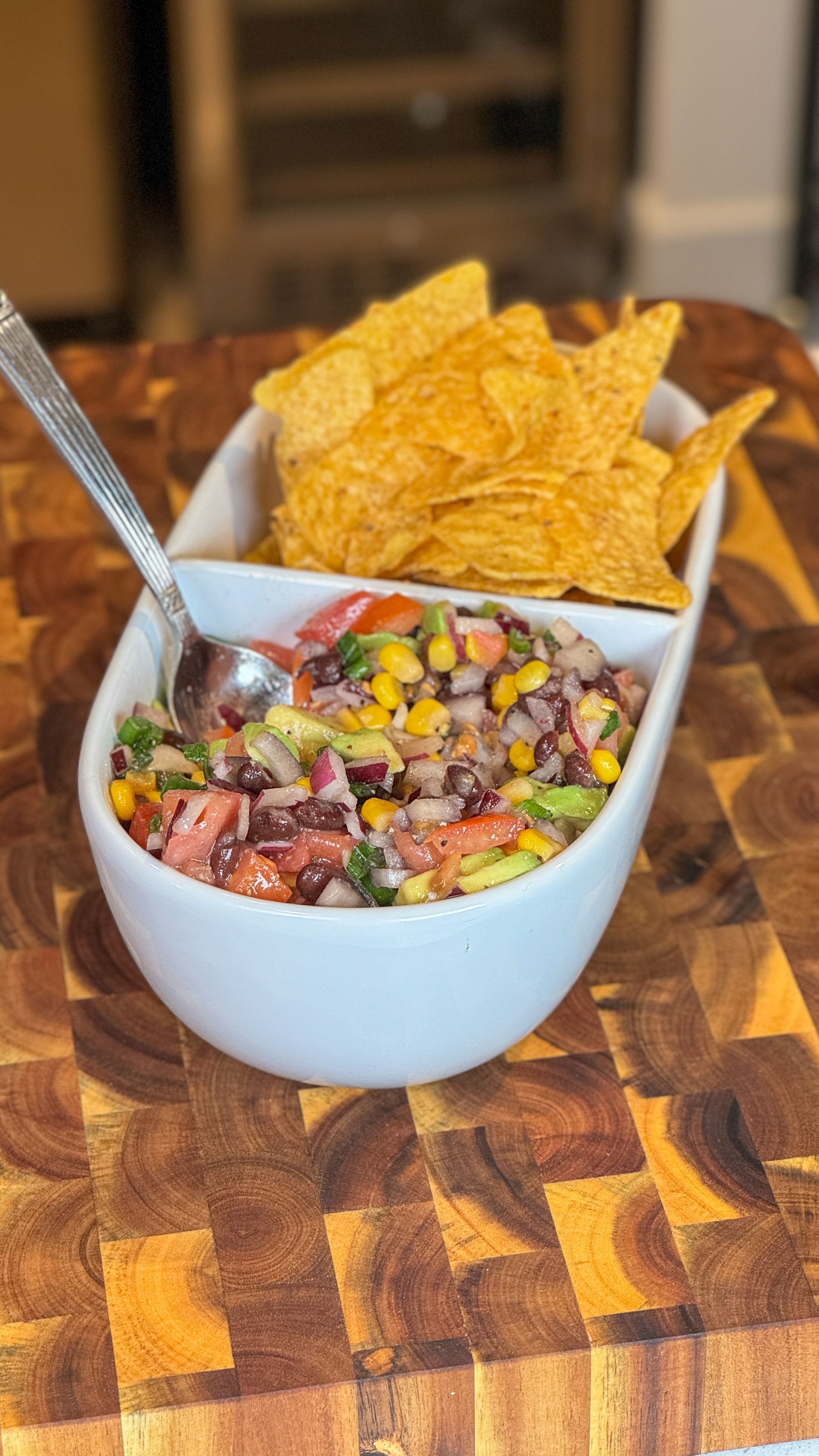 A bowl of salsa and tortilla chips on a wooden cutting board.