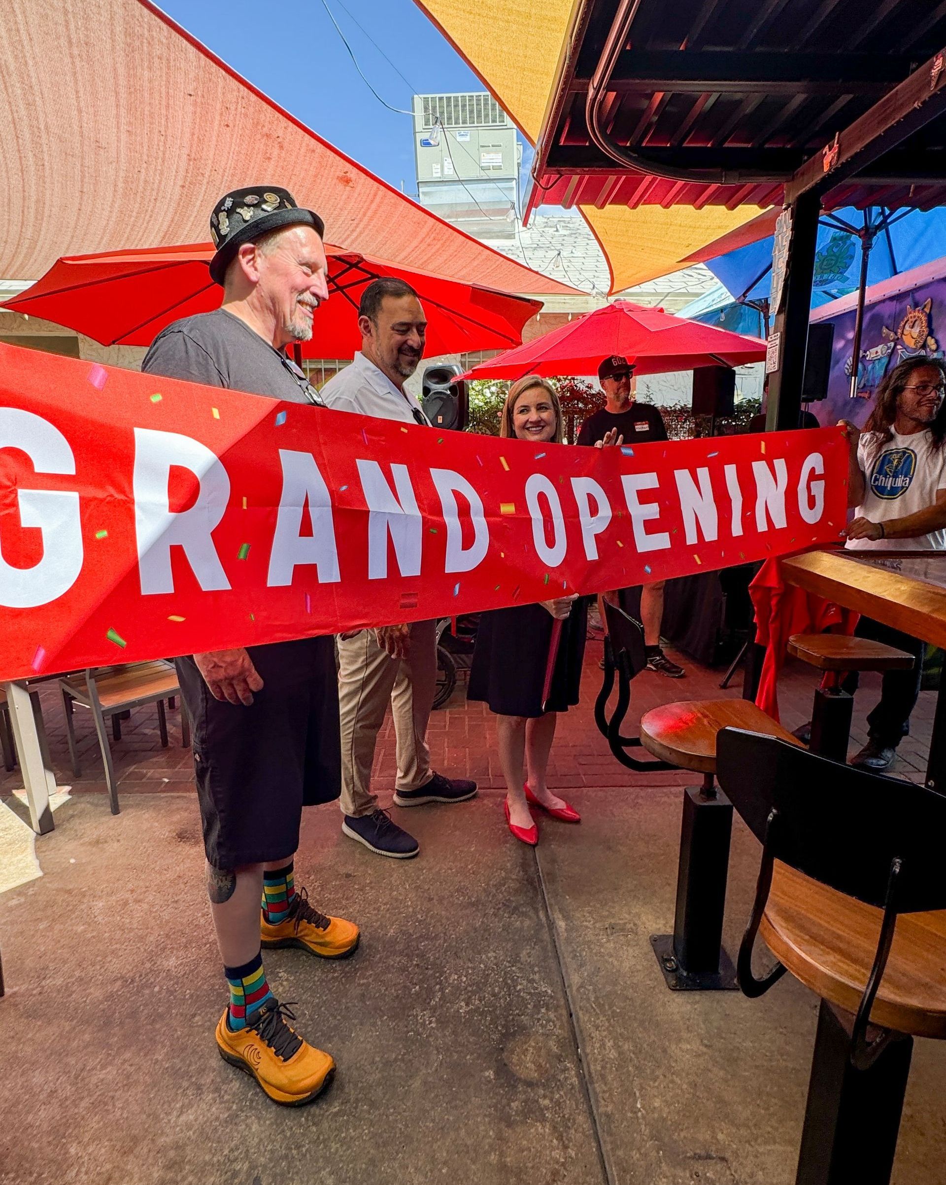 A man is holding a large red banner that says `` grand opening ''.