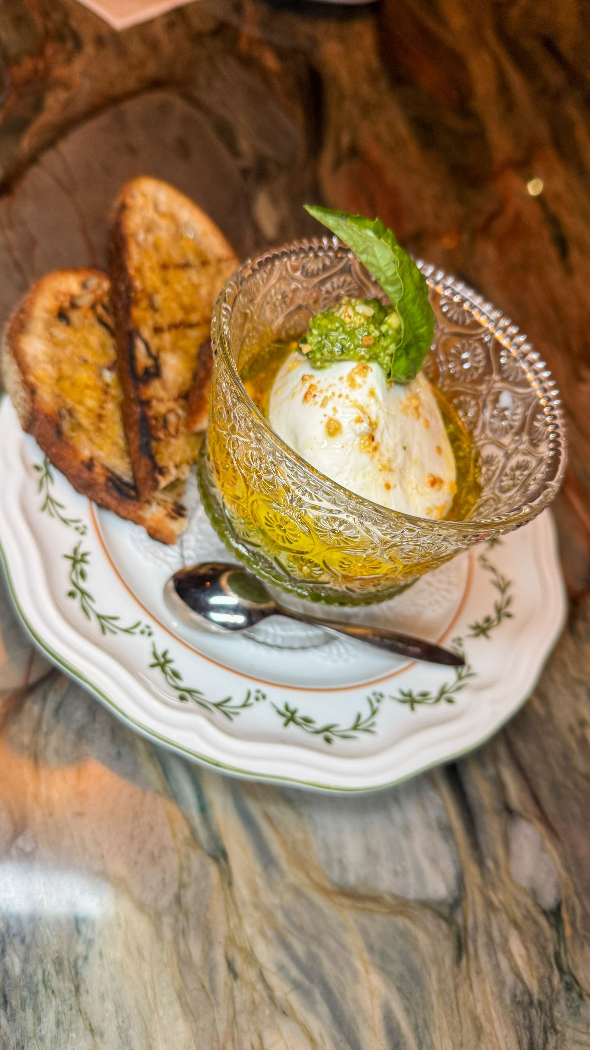 Dessert in a glass bowl topped with mint, beside toasted bread on a patterned plate.