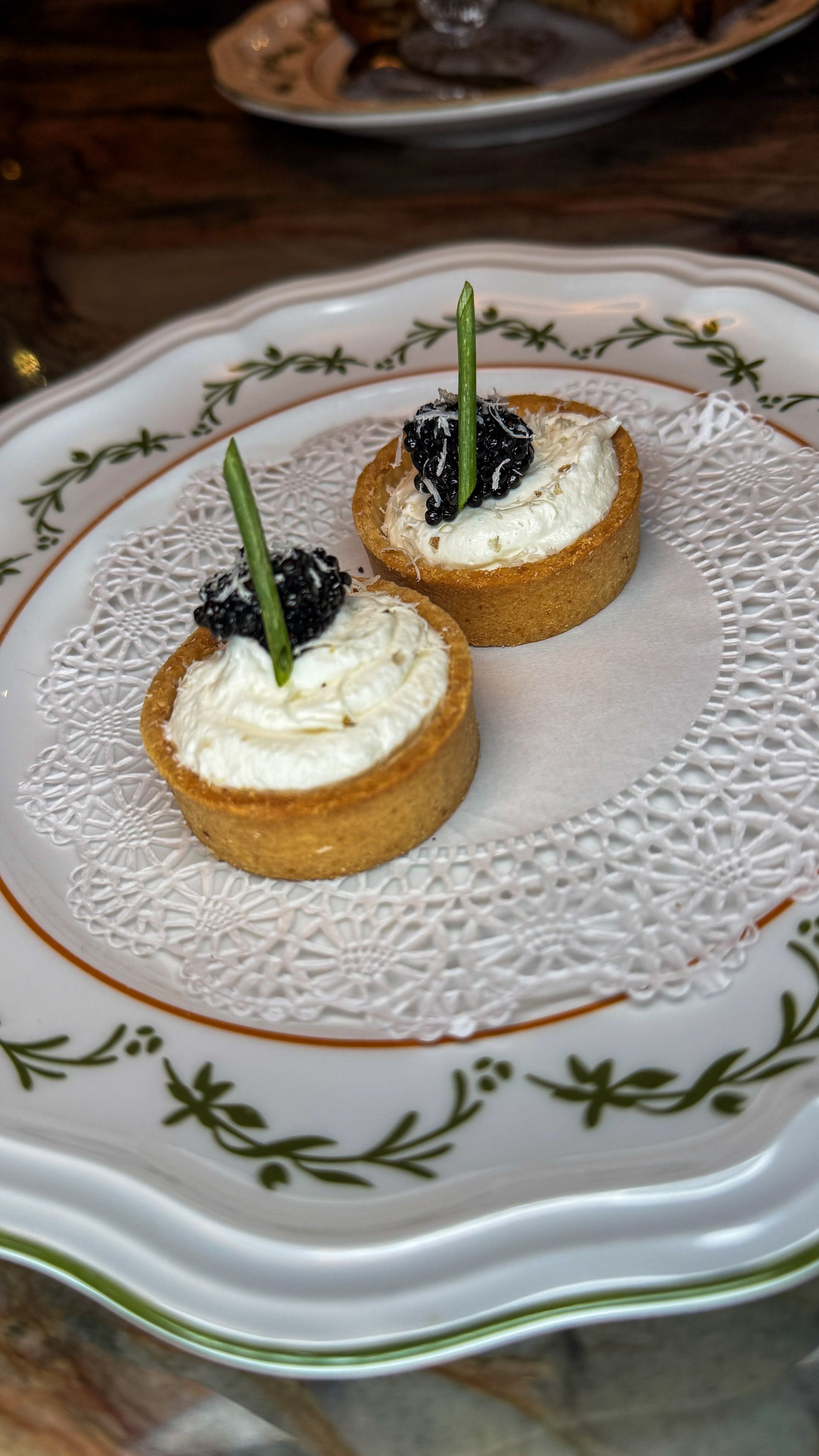 Two small cream-topped pastries on a white decorative plate with green garnish sticks