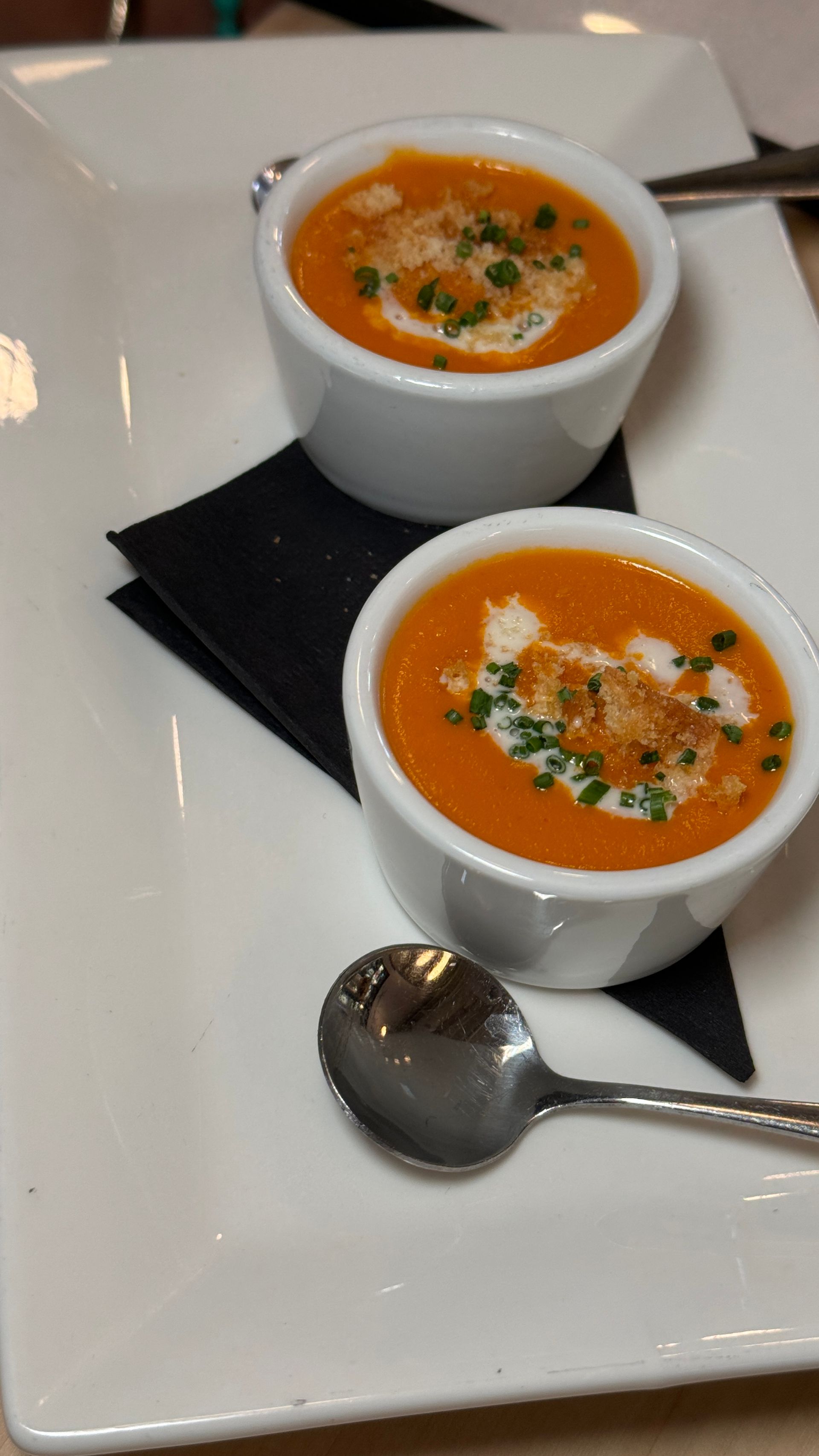 Two bowls of soup on a white plate with a spoon