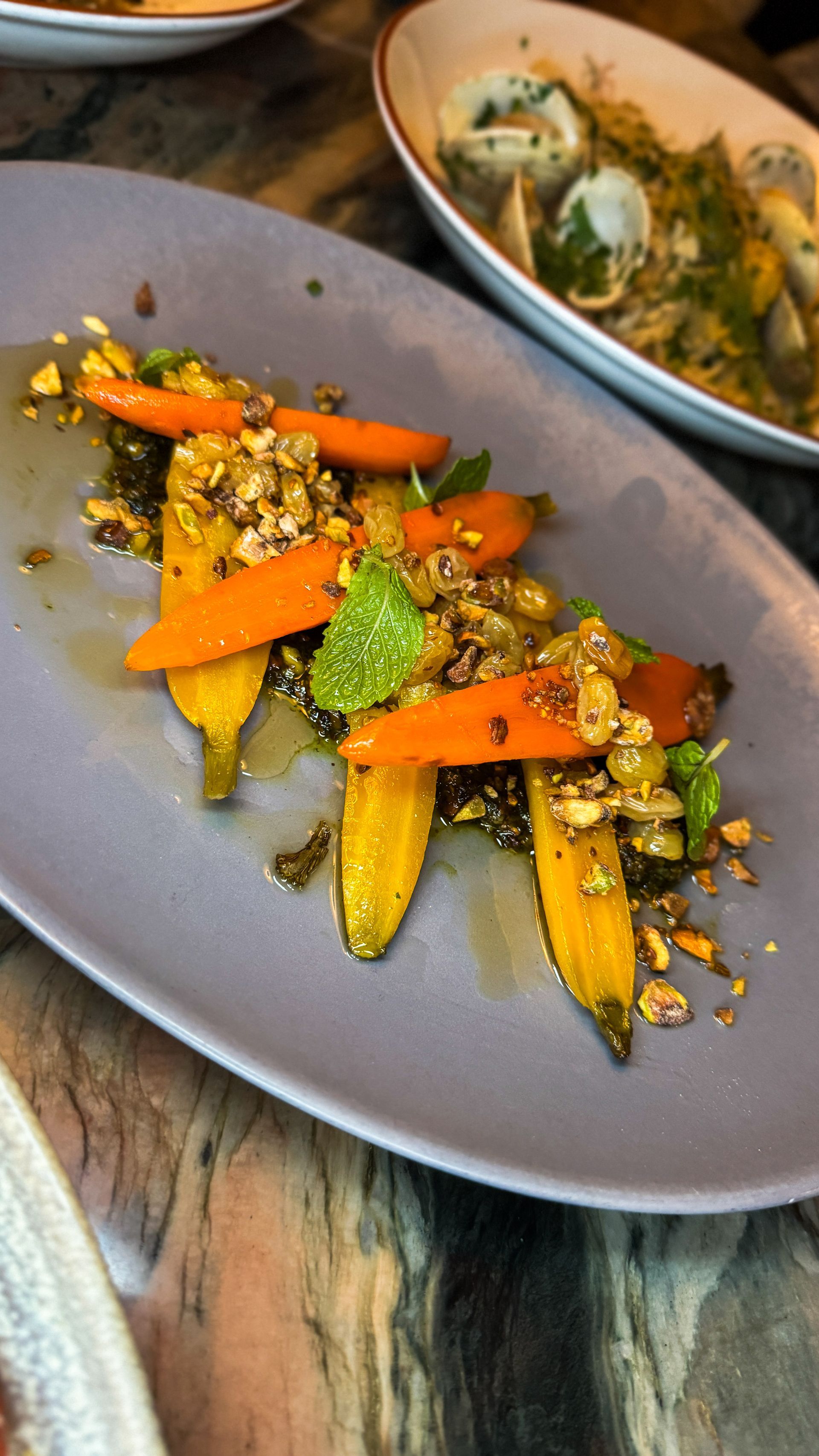 Roasted carrot and vegetable dish on a gray plate, with a second bowl in the background