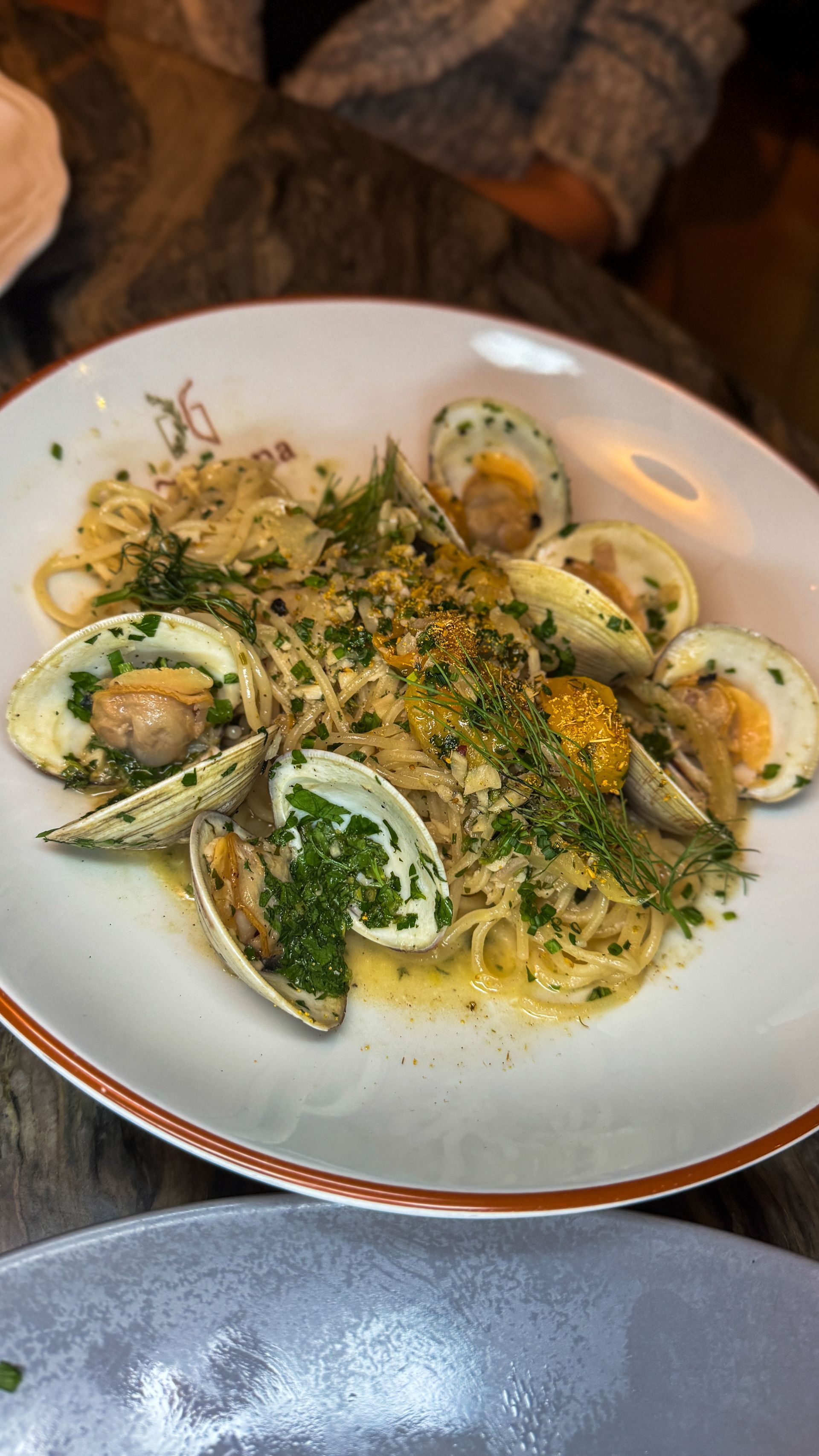 Pasta with clams, herbs, and lemon zest served in a white bowl on a rustic table