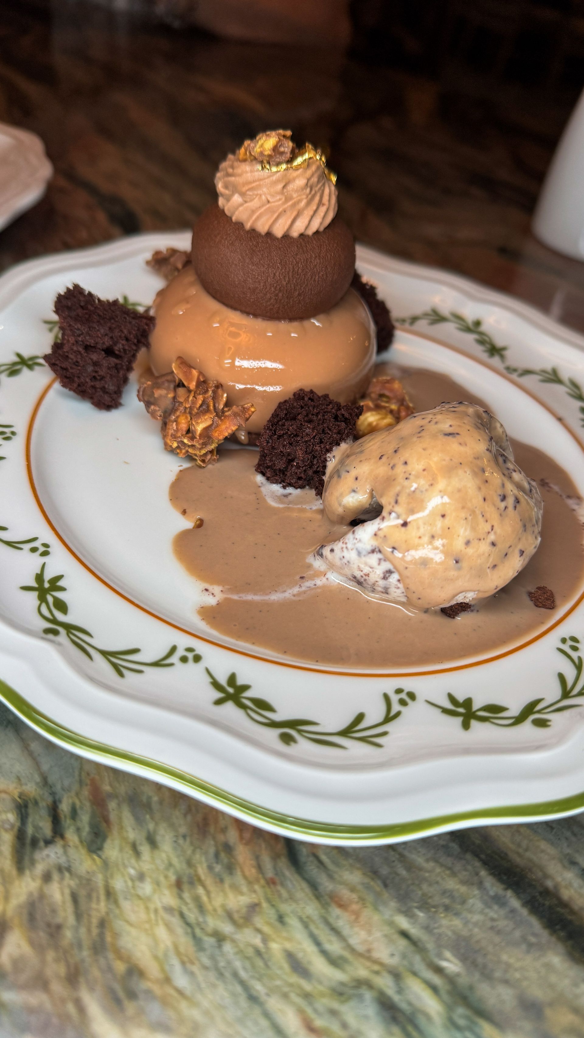 Dessert plate with chocolate tower, caramel mousse, sauce, and a scoop of ice cream on a patterned dish