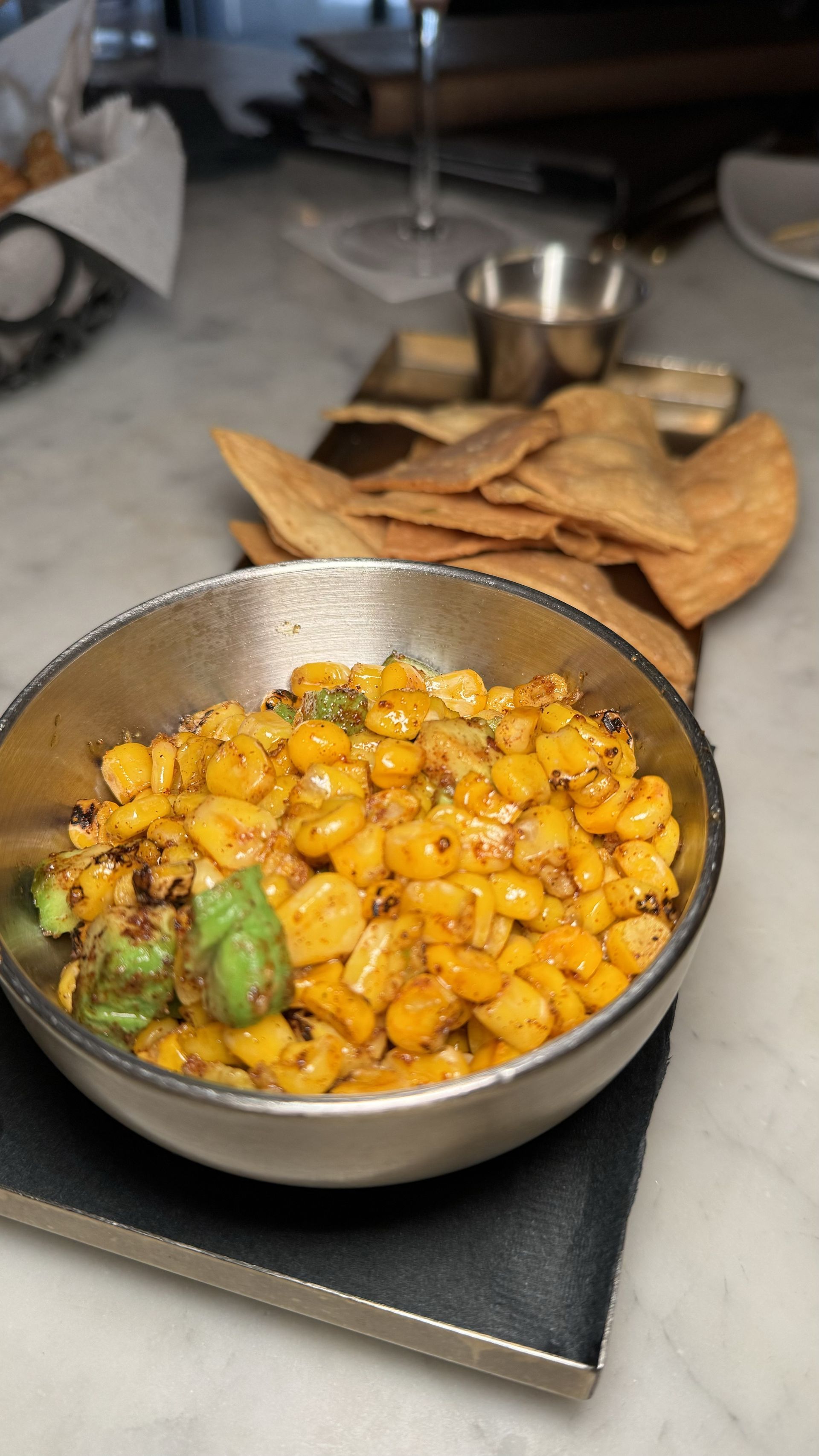 The Beverly - A bowl of corn is sitting on a table next to a tray of chips.
