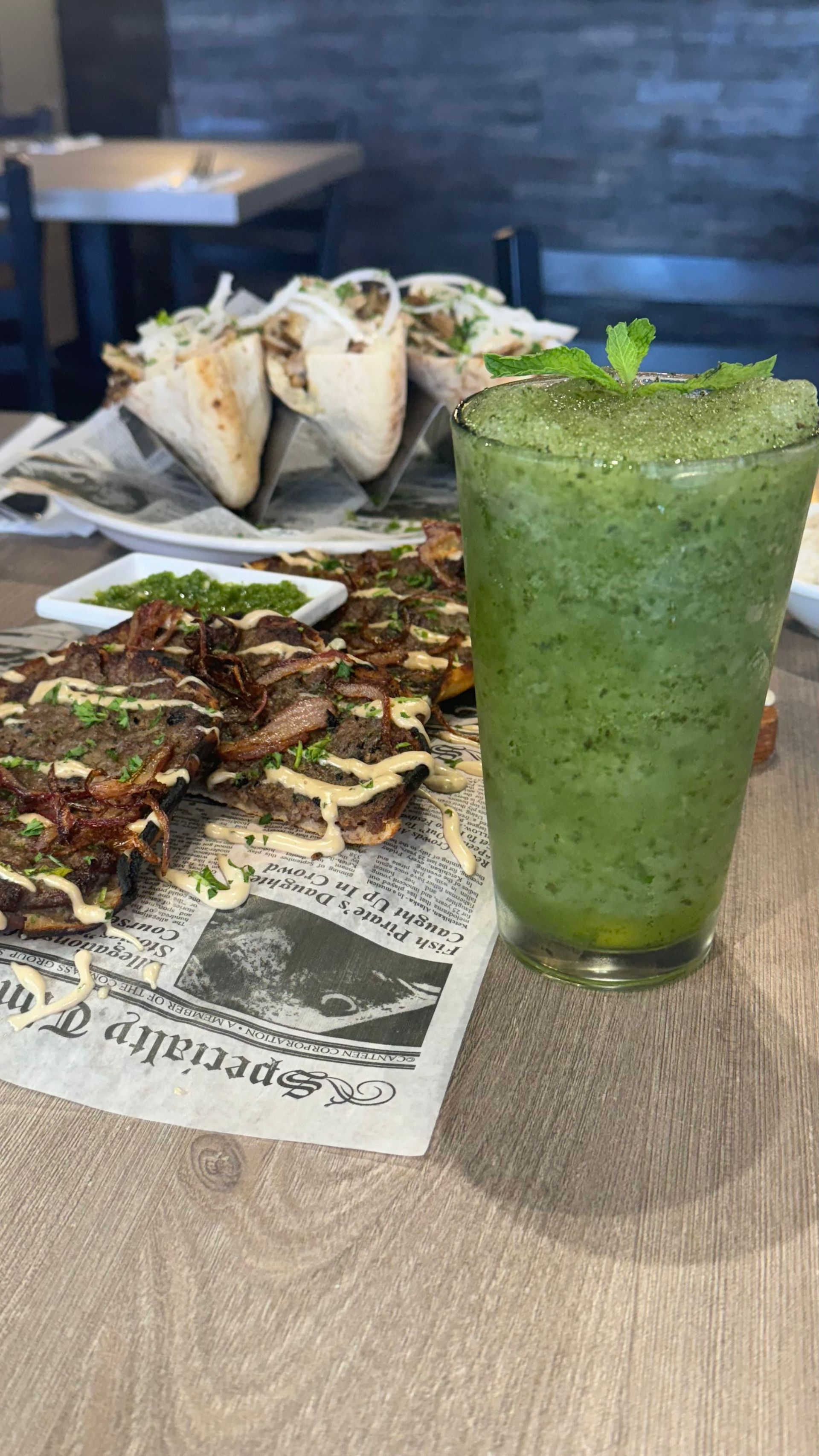 Fata Morgana - A green smoothie is sitting on a table next to a plate of food.